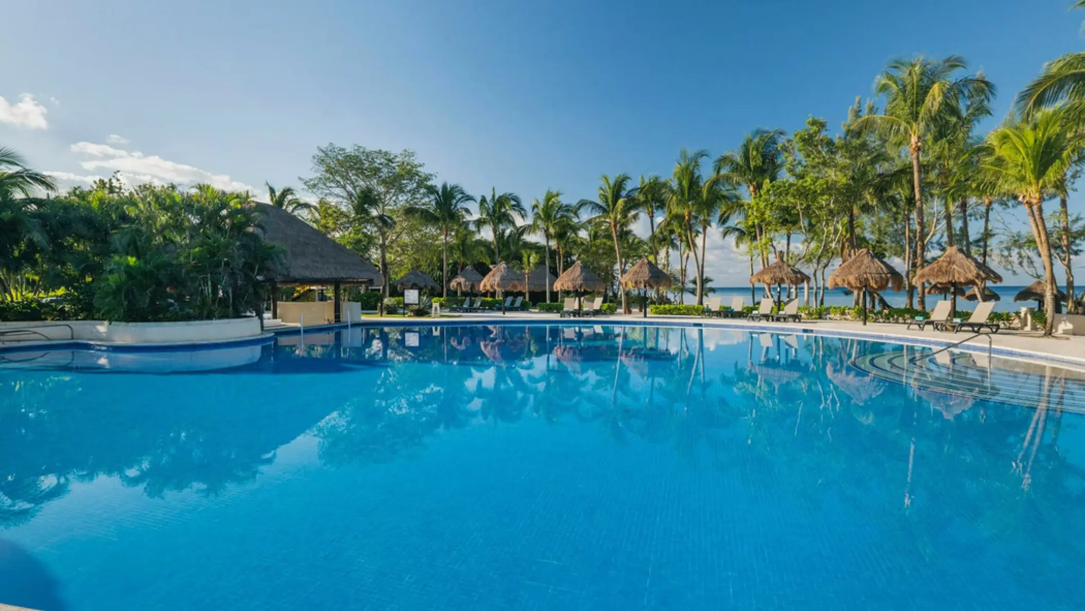 Large swimming pool surrounded by palm trees and palapas at Iberostar Waves Cozumel