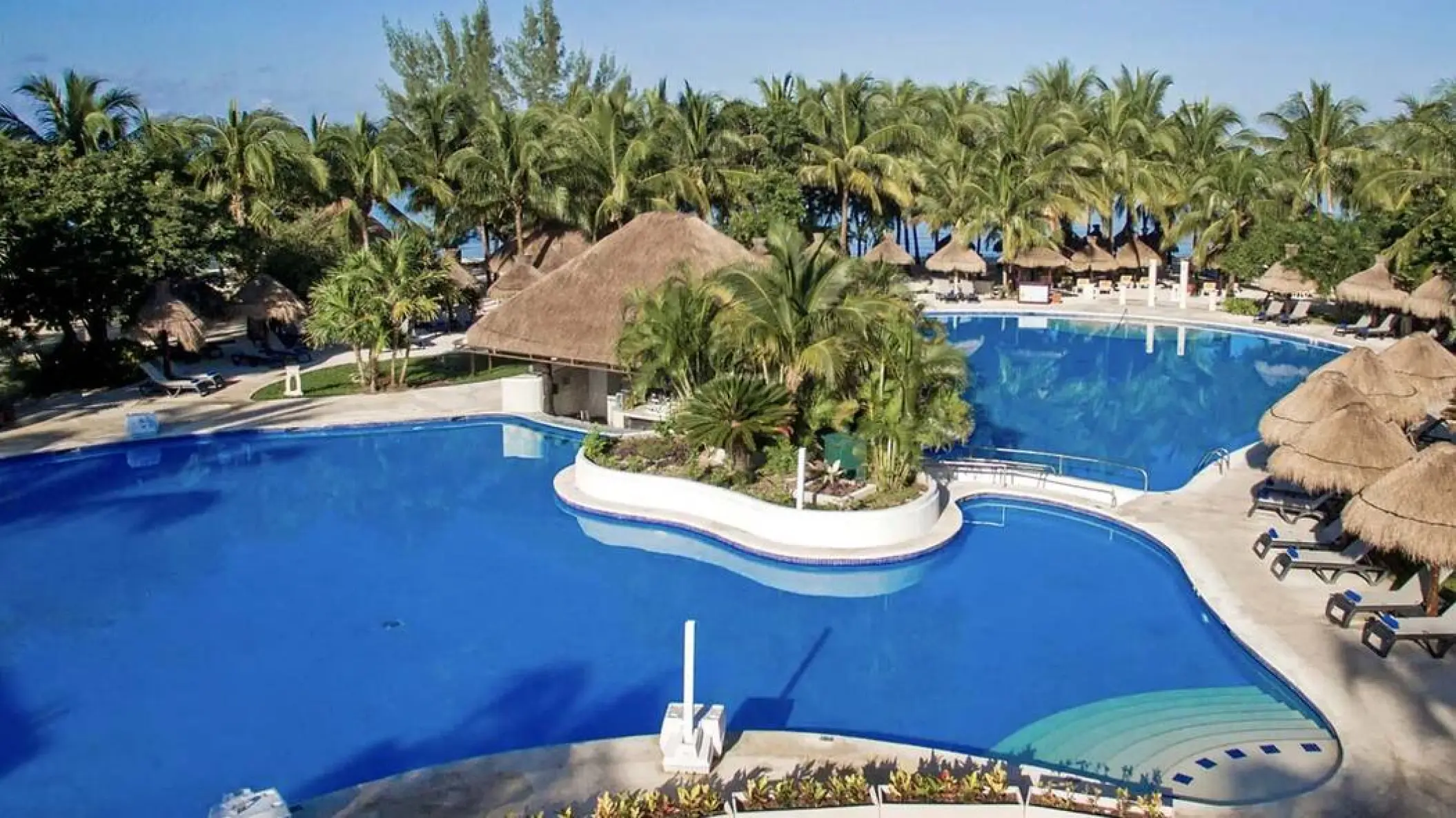 Large outdoor swimming pool with a swim-up bar and palm trees at Iberostar Waves Cozumel