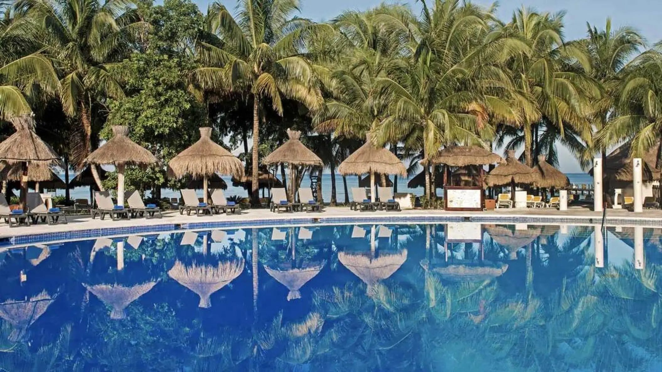 Palm trees and thatched umbrellas reflected in the swimming pool at Iberostar Waves Cozumel