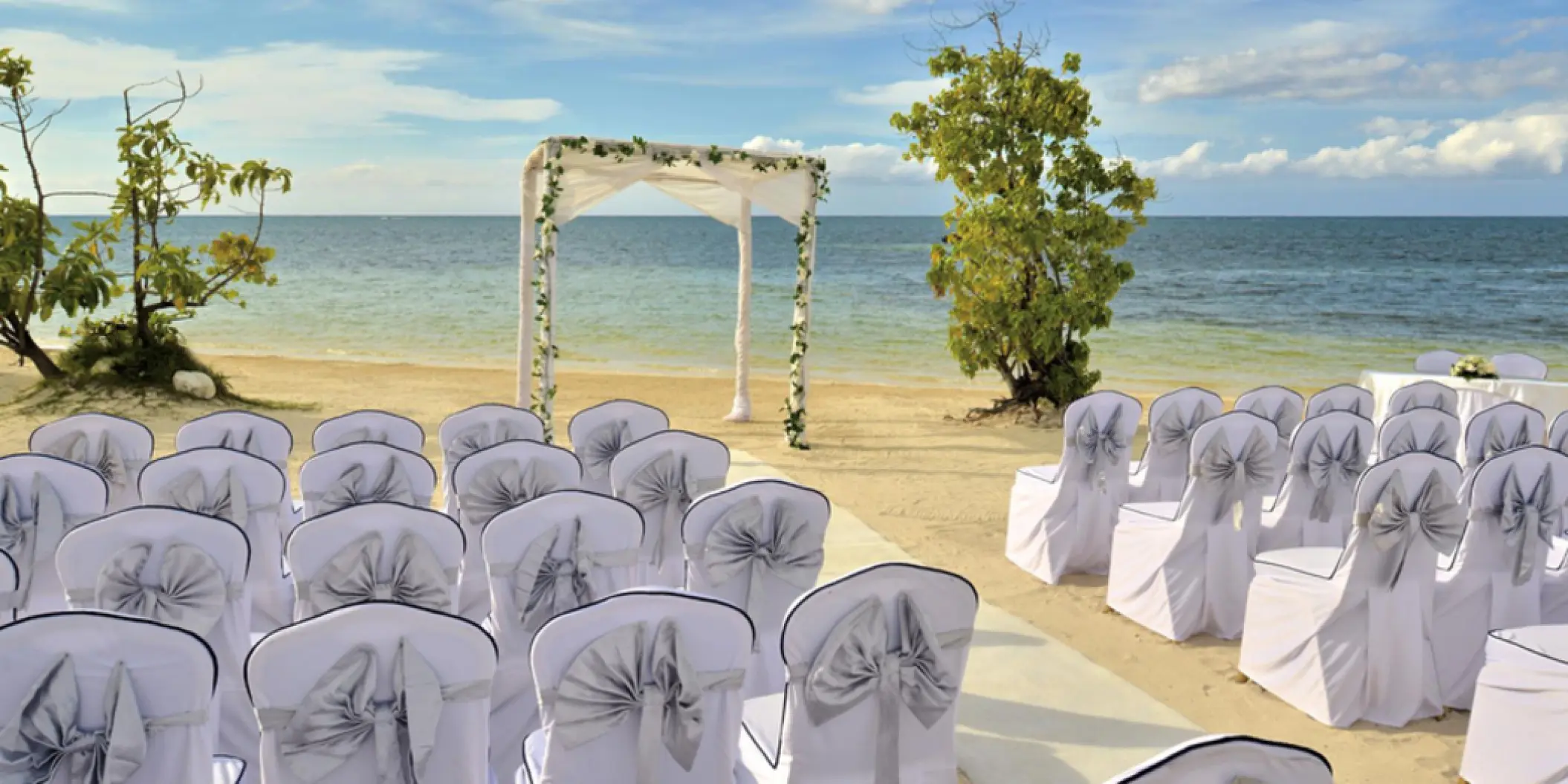 Beachfront wedding ceremony setup with white floral arch at Iberostar Waves Rose Hall Beach, Montego Bay