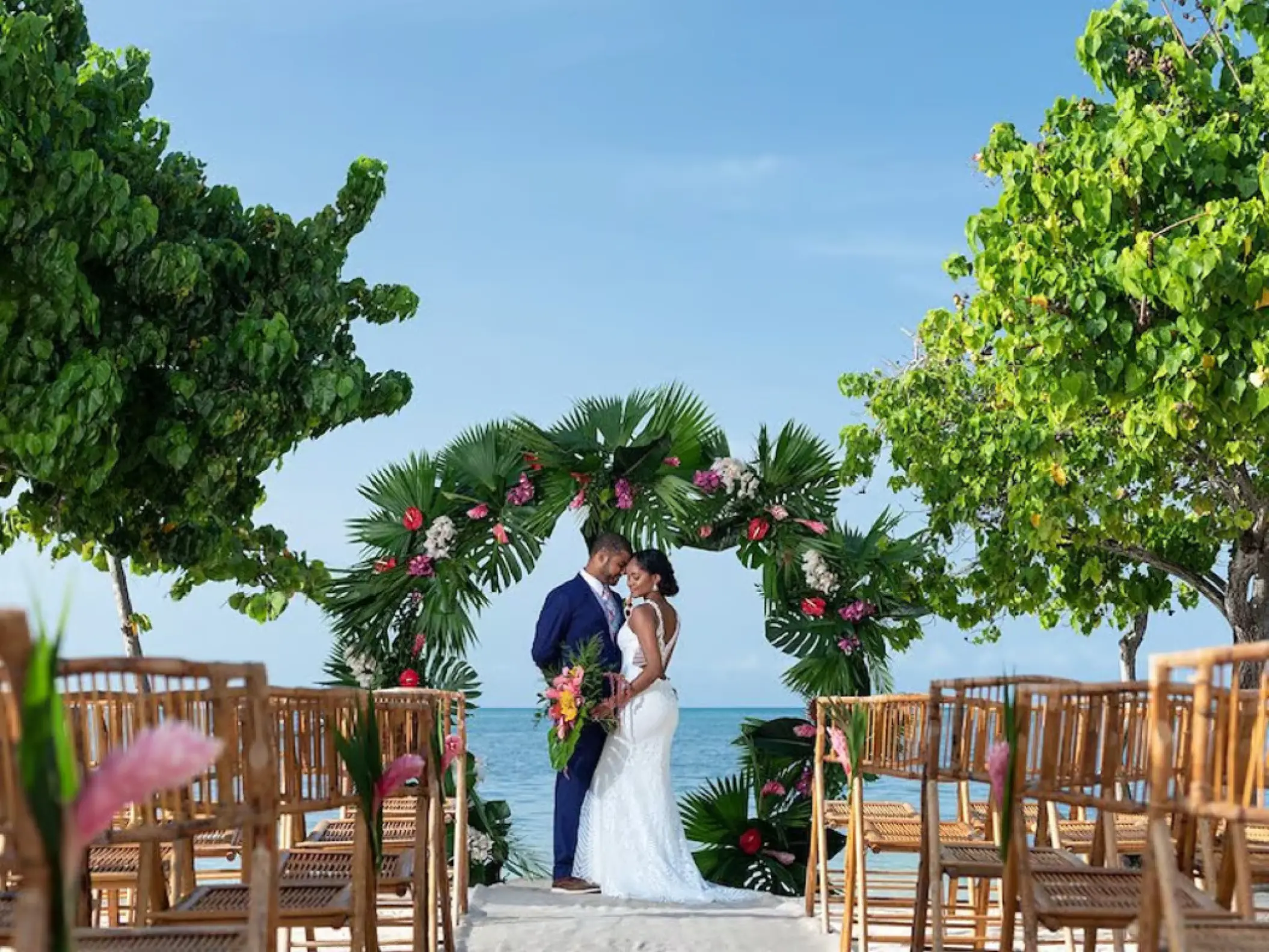 Bride and groom under a tropical floral arch at an Iberostar Rose Hall Beach ceremony, Montego Bay