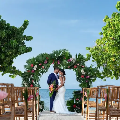 Bride and groom under a tropical floral arch at an Iberostar Rose Hall Beach ceremony, Montego Bay