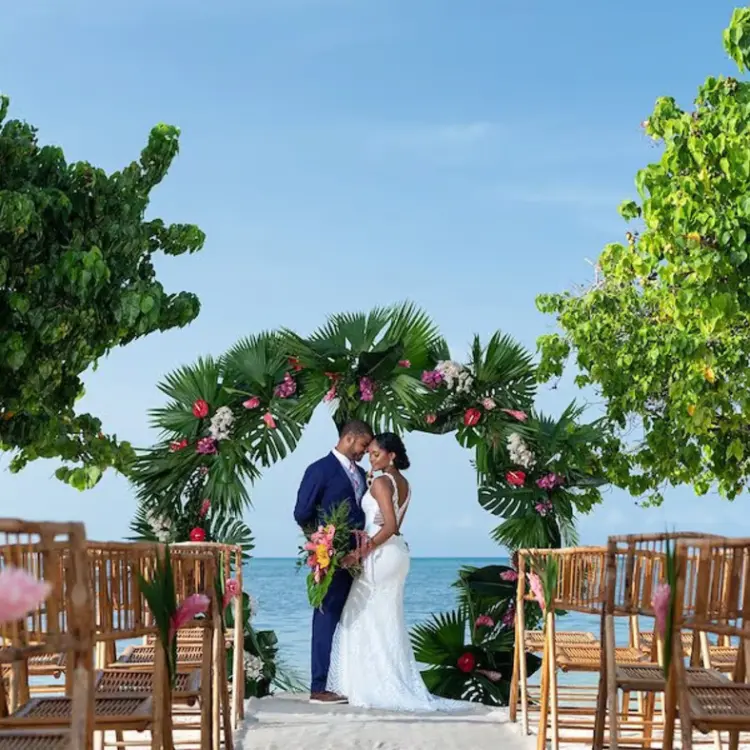 Bride and groom under a tropical floral arch at an Iberostar Rose Hall Beach ceremony, Montego Bay