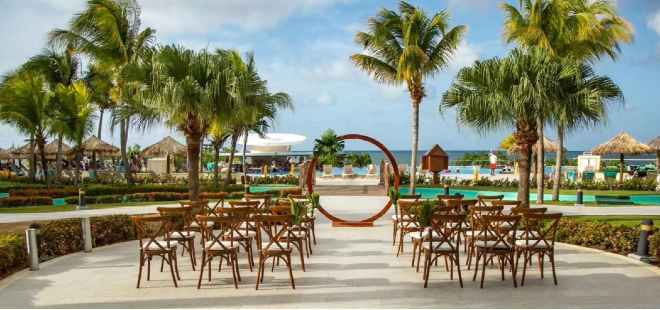Outdoor wedding ceremony with a circular arch and wooden chairs at Iberostar Waves Rose Hall Beach, Montego Bay