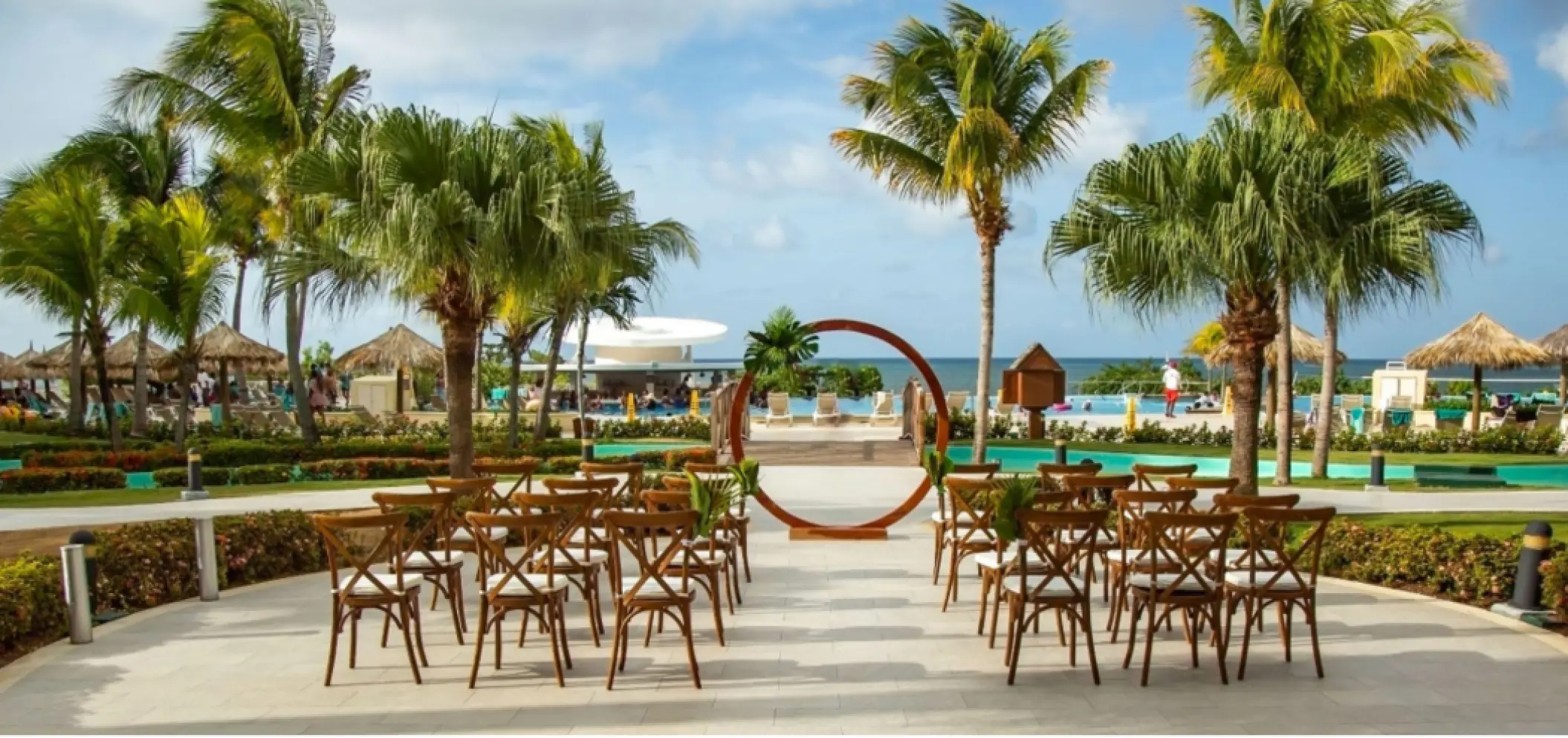 Outdoor wedding ceremony with a circular arch and wooden chairs at Iberostar Waves Rose Hall Beach, Montego Bay
