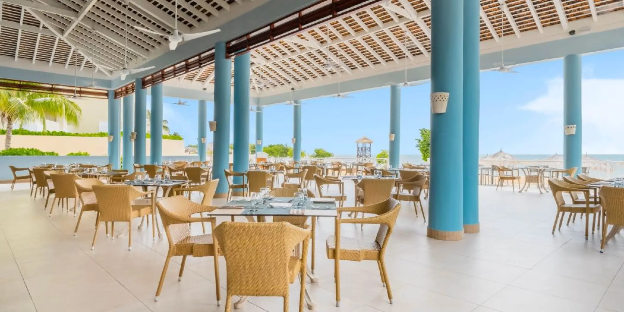 Open-air oceanfront restaurant with wicker chairs and blue columns at Iberostar Rose Hall Beach, Montego Bay