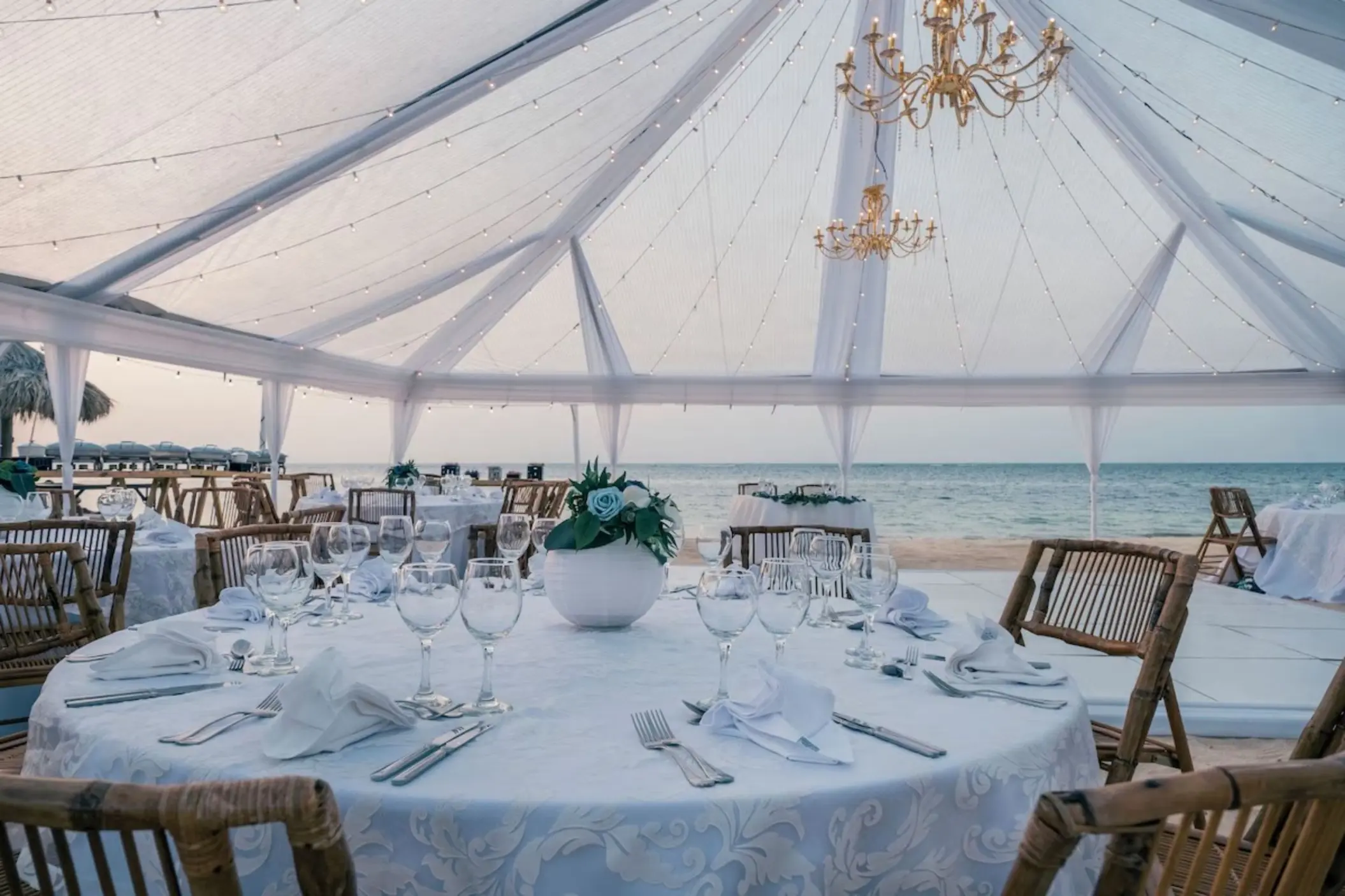Beachfront wedding reception under a clear tent with chandeliers at JOIA Rose Hall, Montego Bay