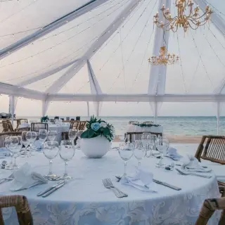 Beachfront wedding reception under a clear tent with chandeliers at JOIA Rose Hall, Montego Bay
