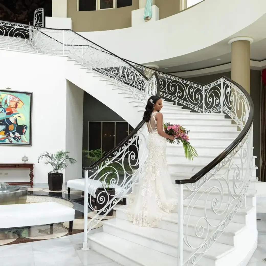 Bride holding a bouquet on the white grand staircase at JOIA Rose Hall by Iberostar, Montego Bay