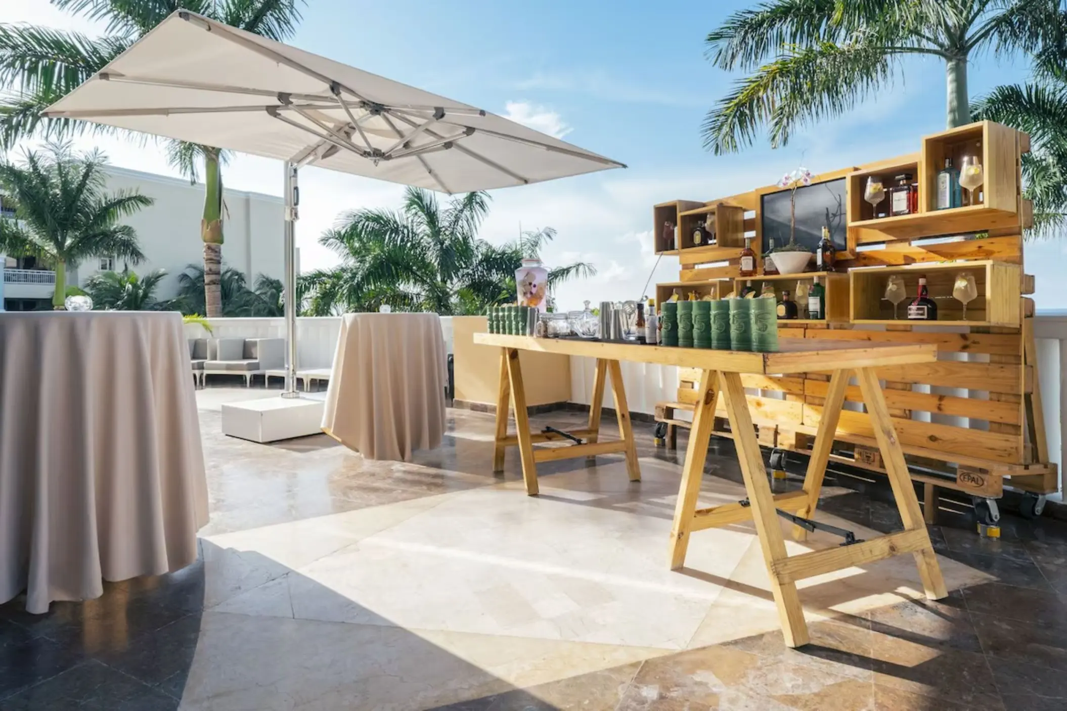 Outdoor wedding reception bar with wooden pallets and high-top tables at JOIA Rose Hall, Montego Bay