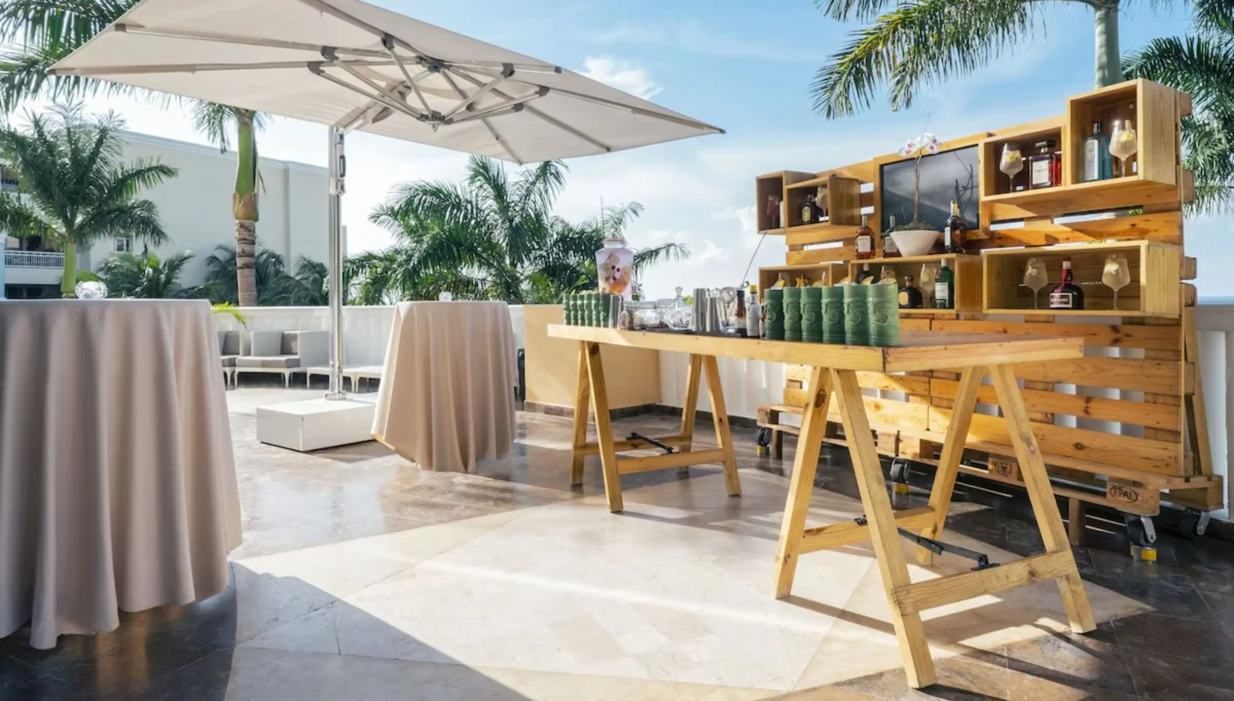 Outdoor wedding reception bar with wooden pallets and high-top tables at JOIA Rose Hall, Montego Bay