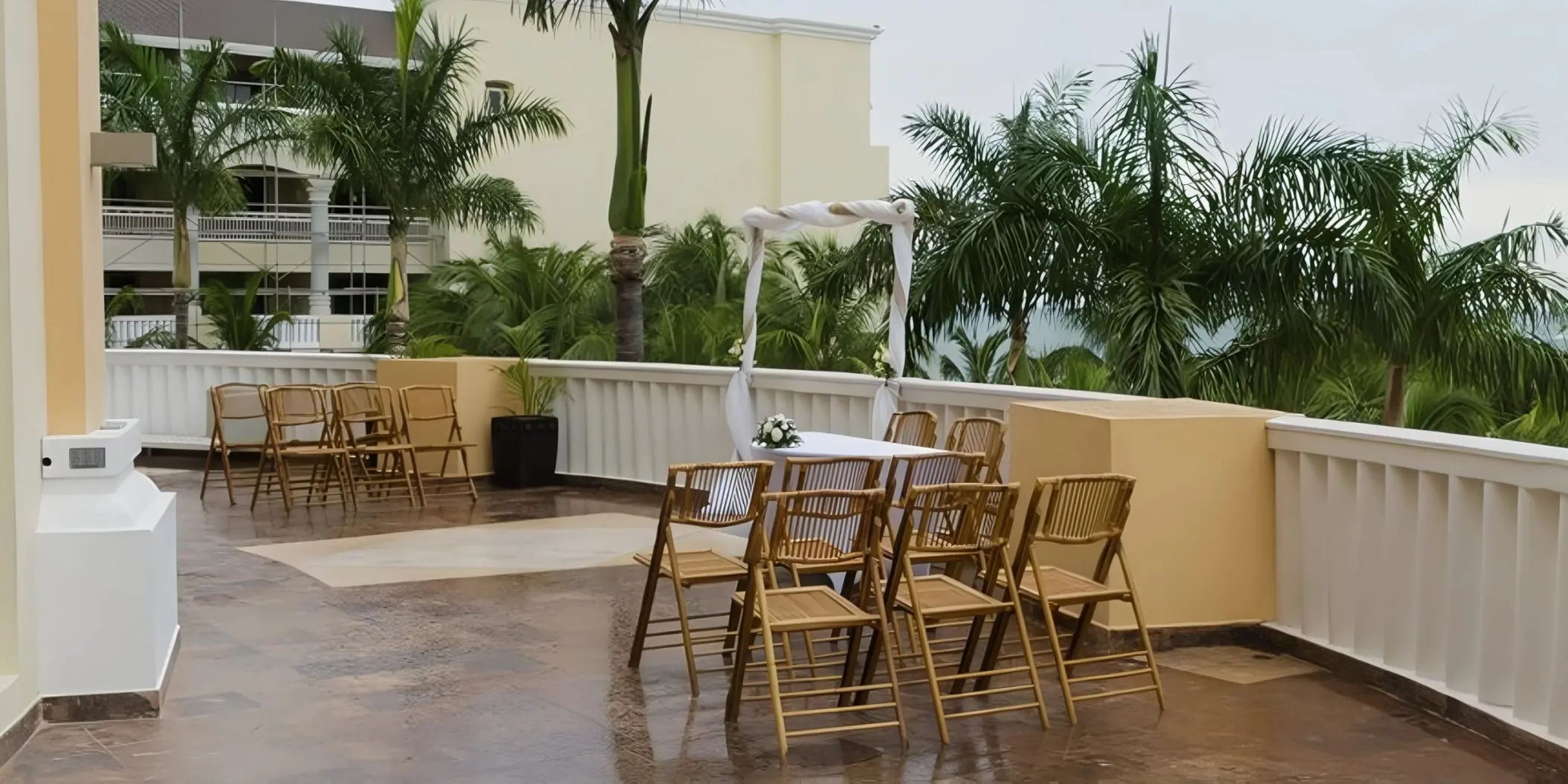 Lobby terrace wedding ceremony with wooden chairs and white fabric arch at JOIA Rose Hall, Montego Bay