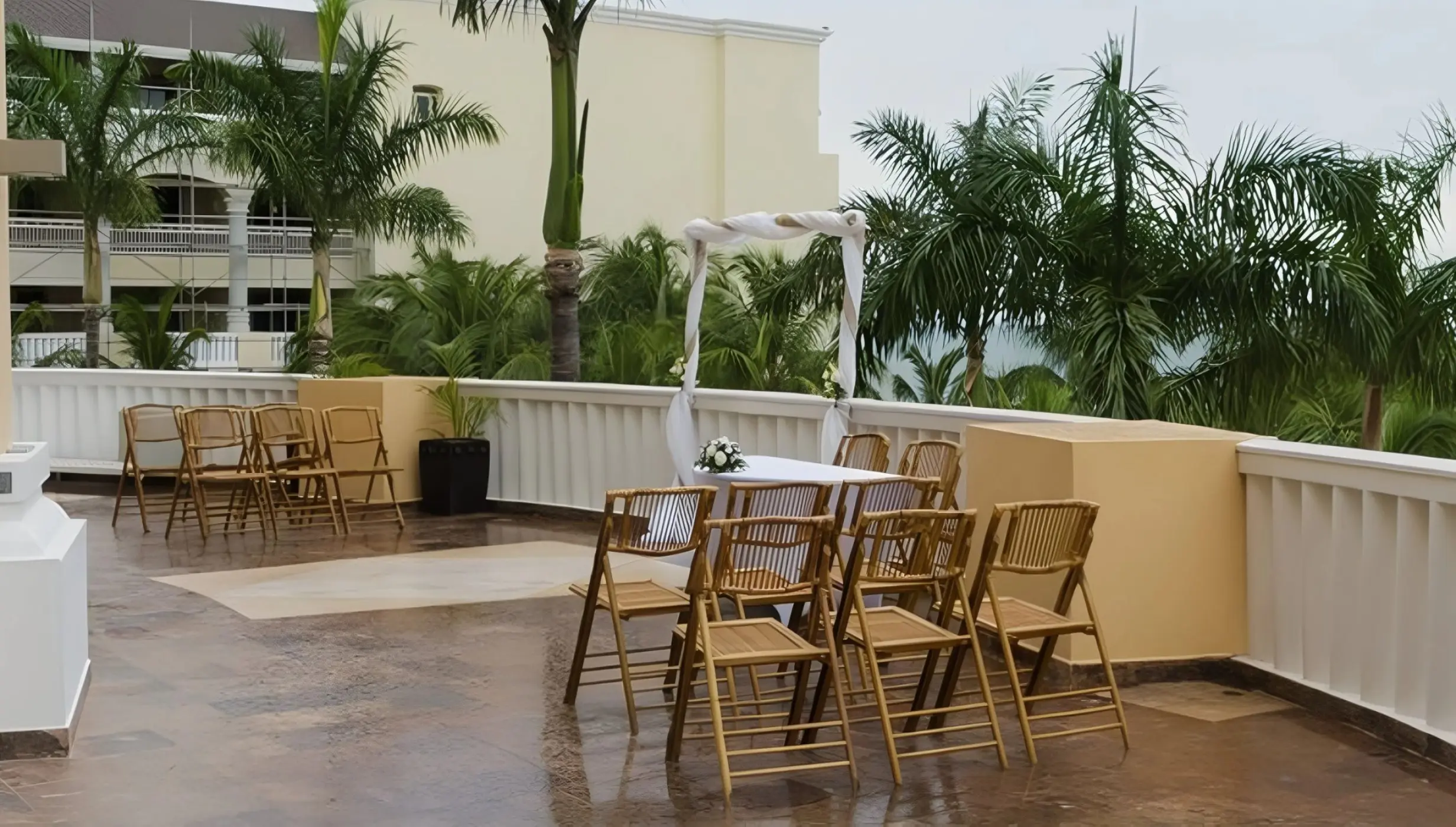 Lobby terrace wedding ceremony with wooden chairs and white fabric arch at JOIA Rose Hall, Montego Bay