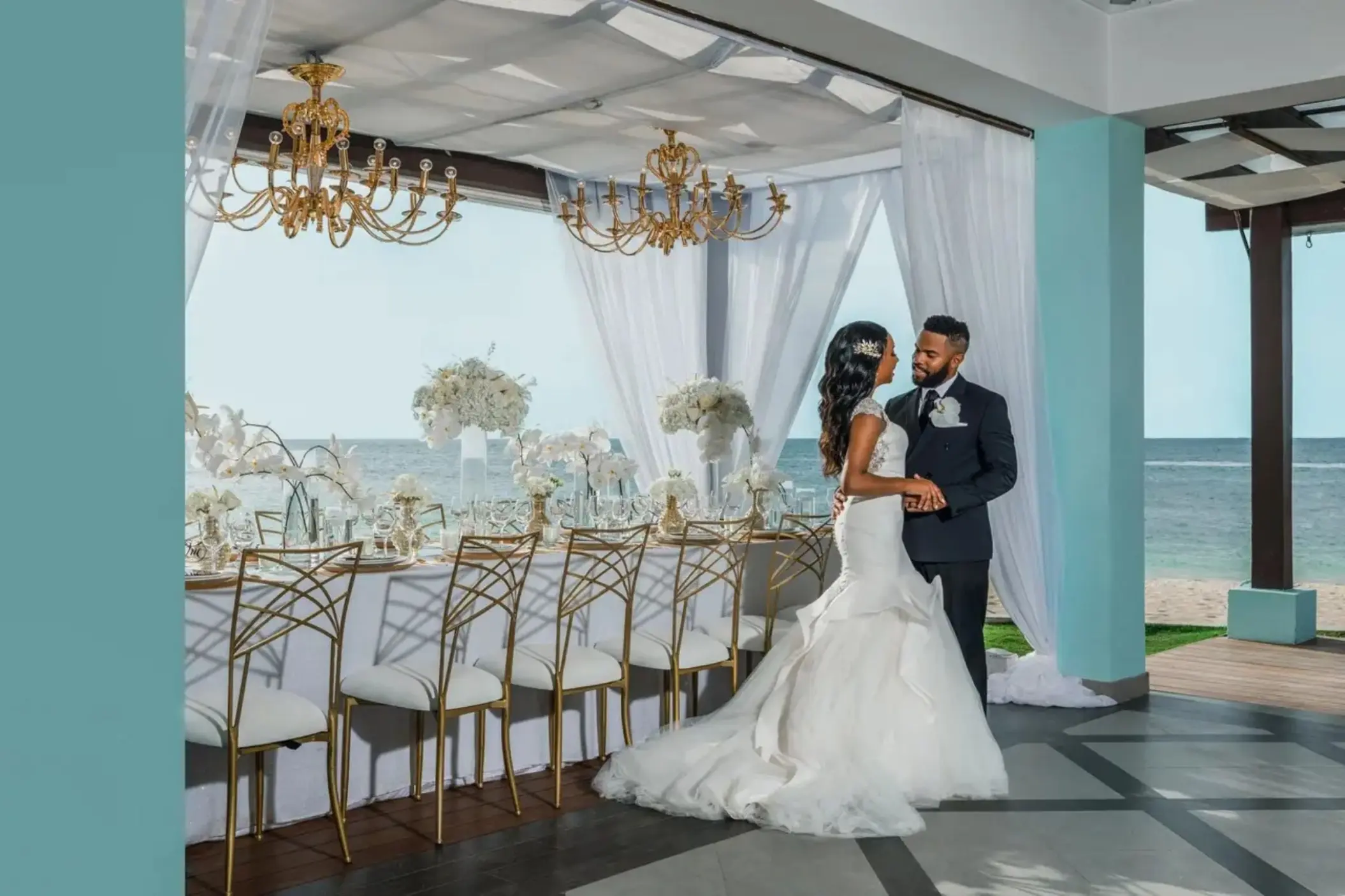 Bride and groom at a beach reception with gold chairs at JOIA Rose Hall, Montego Bay