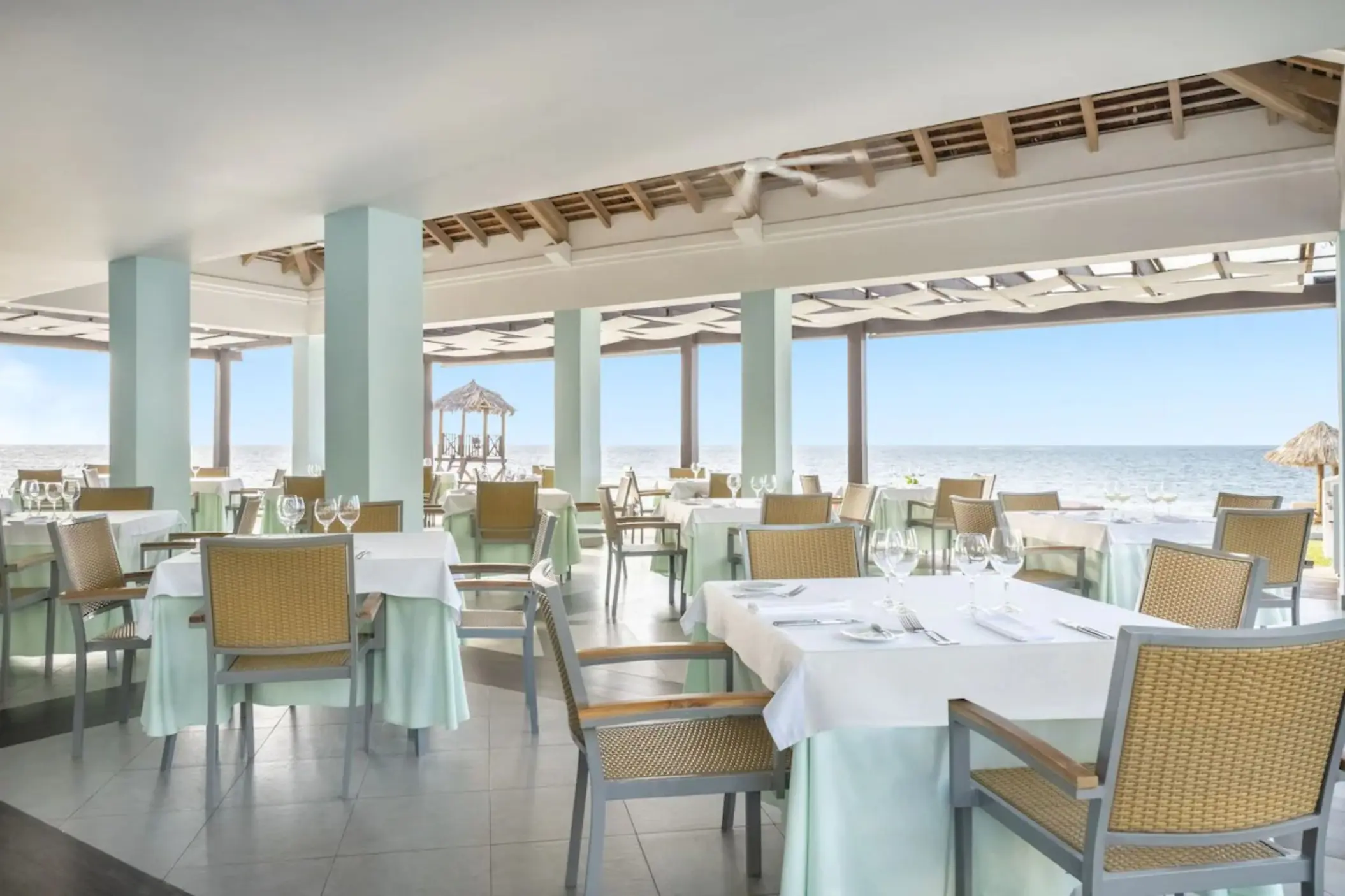 Port Maria beach restaurant with white-clothed tables and ocean views at JOIA Rose Hall by Iberostar, Montego Bay