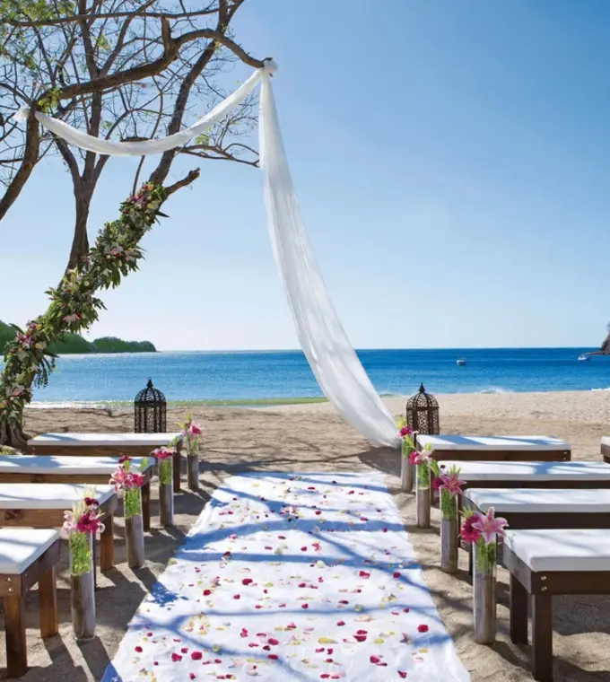 Beachfront wedding ceremony with white draped fabric and wooden benches at JW Marriott Costa Elena, El Jobo