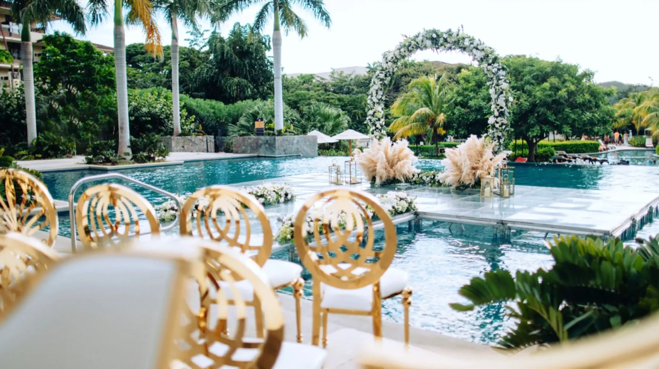 Poolside wedding ceremony with a circular floral arch and gold chairs at JW Marriott Costa Elena, El Jobo