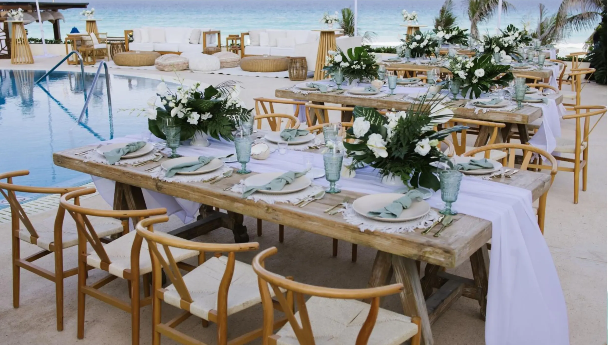 Poolside wedding reception with wooden tables and white floral centerpieces at Live Aqua Beach Cancun
