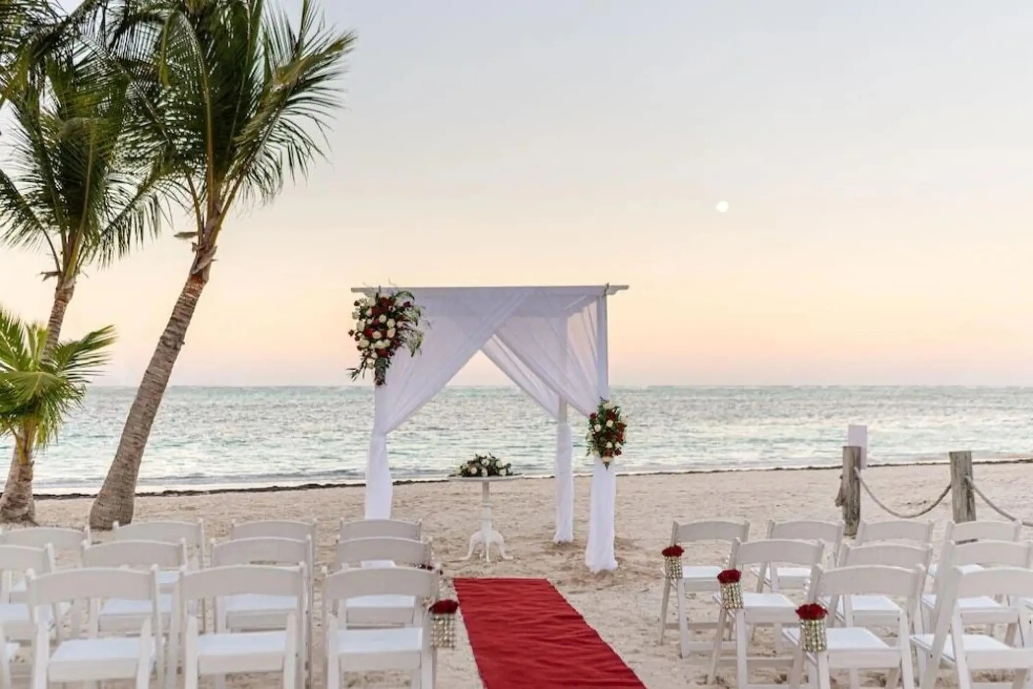 Beachfront wedding ceremony with white draped arch and red aisle runner at Lopesan Costa Bavaro, Punta Cana