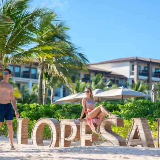 A couple posing with the wooden Lopesan sign on the beach at Lopesan Costa Bavaro, Punta Cana