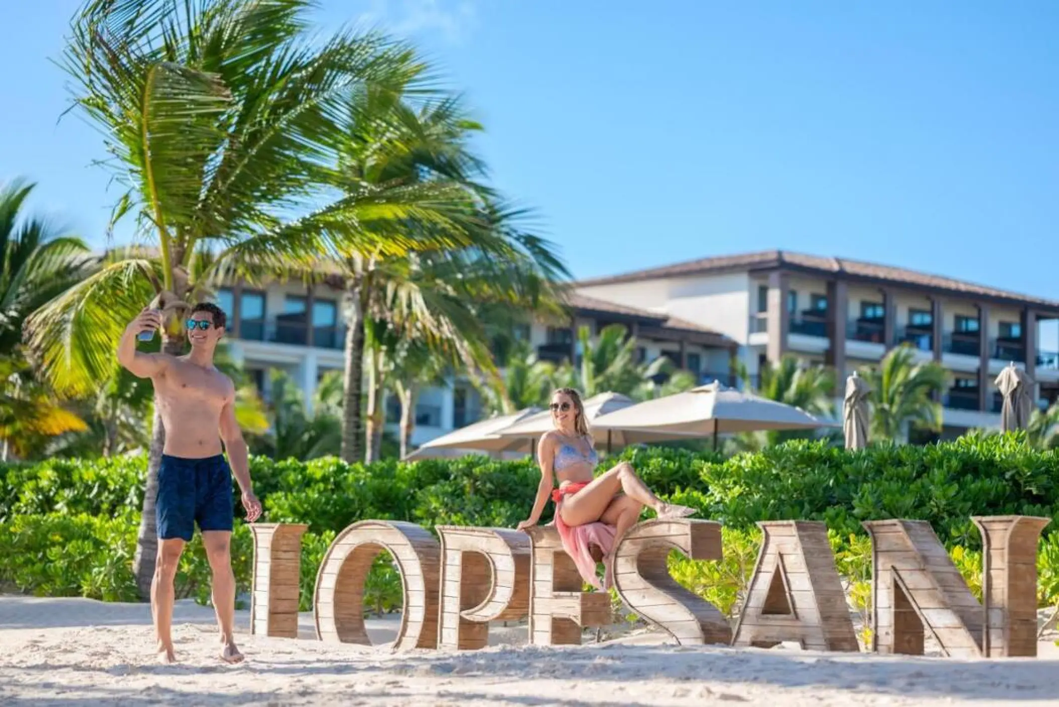 A couple posing with the wooden Lopesan sign on the beach at Lopesan Costa Bavaro, Punta Cana