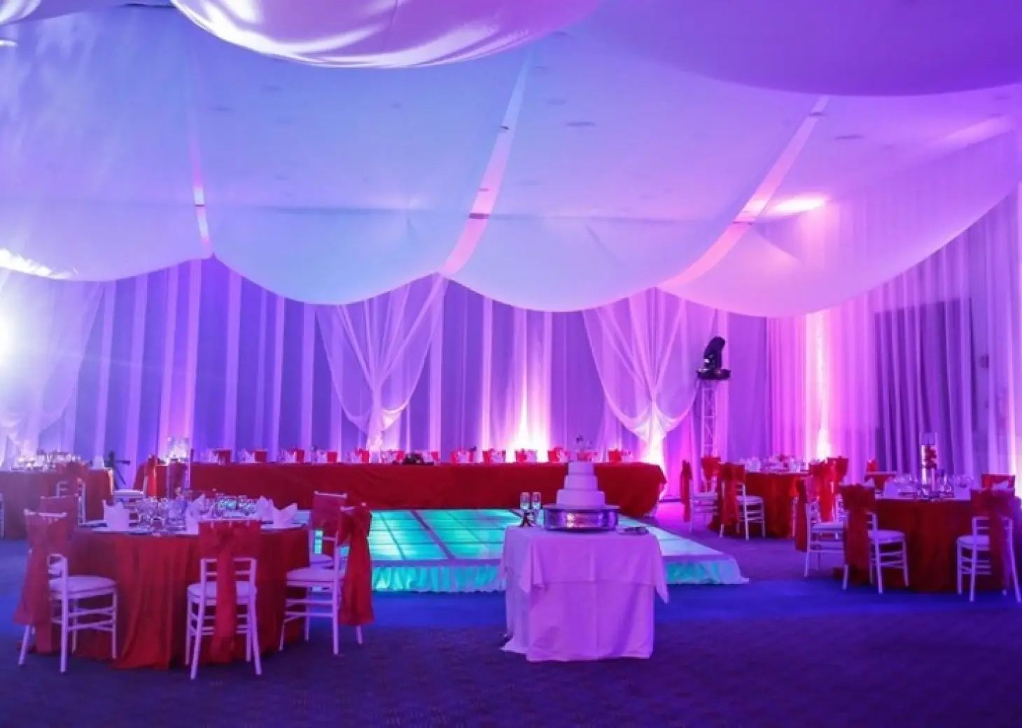 Indoor wedding reception with purple lighting and red table linens at Majestic Colonial, Punta Cana