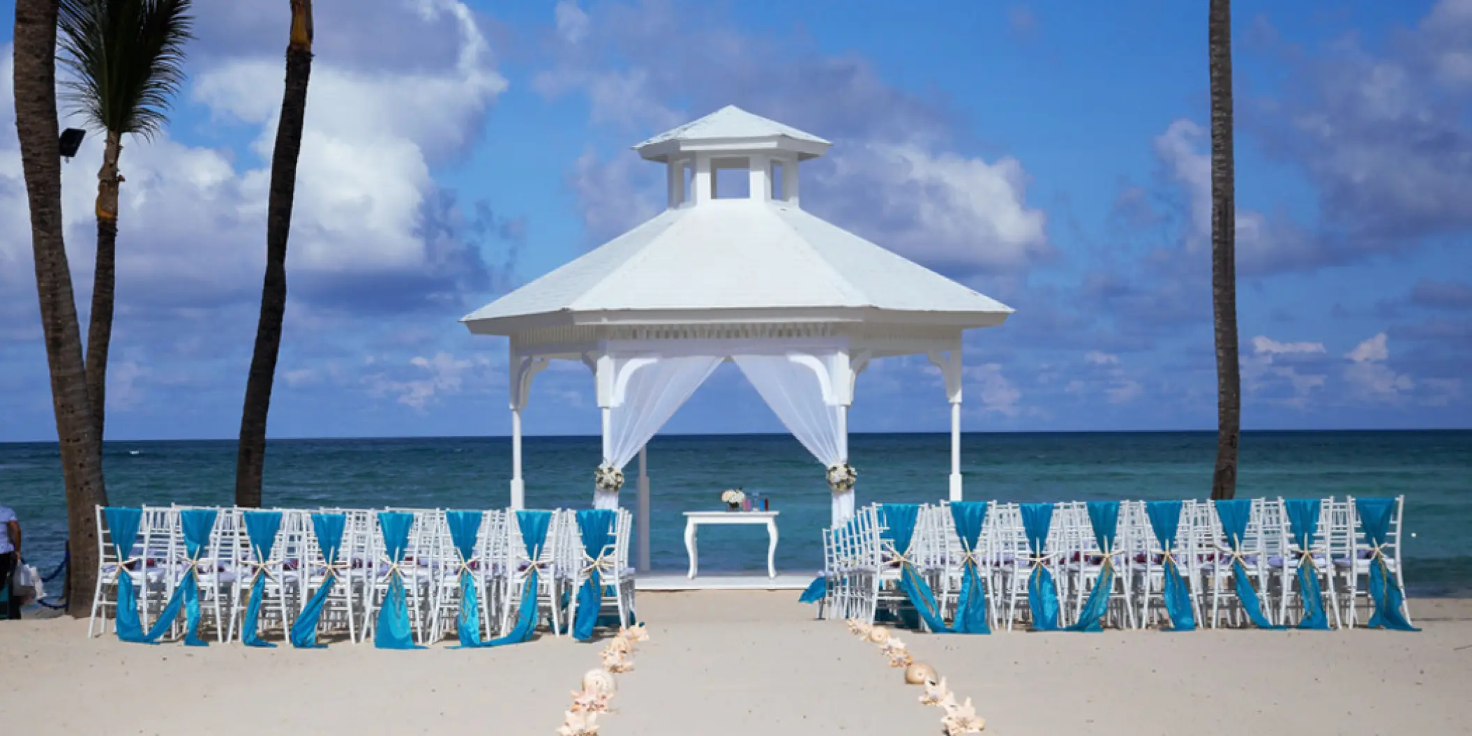 Beach gazebo wedding ceremony with white chairs and teal sashes at Majestic Colonial, Punta Cana