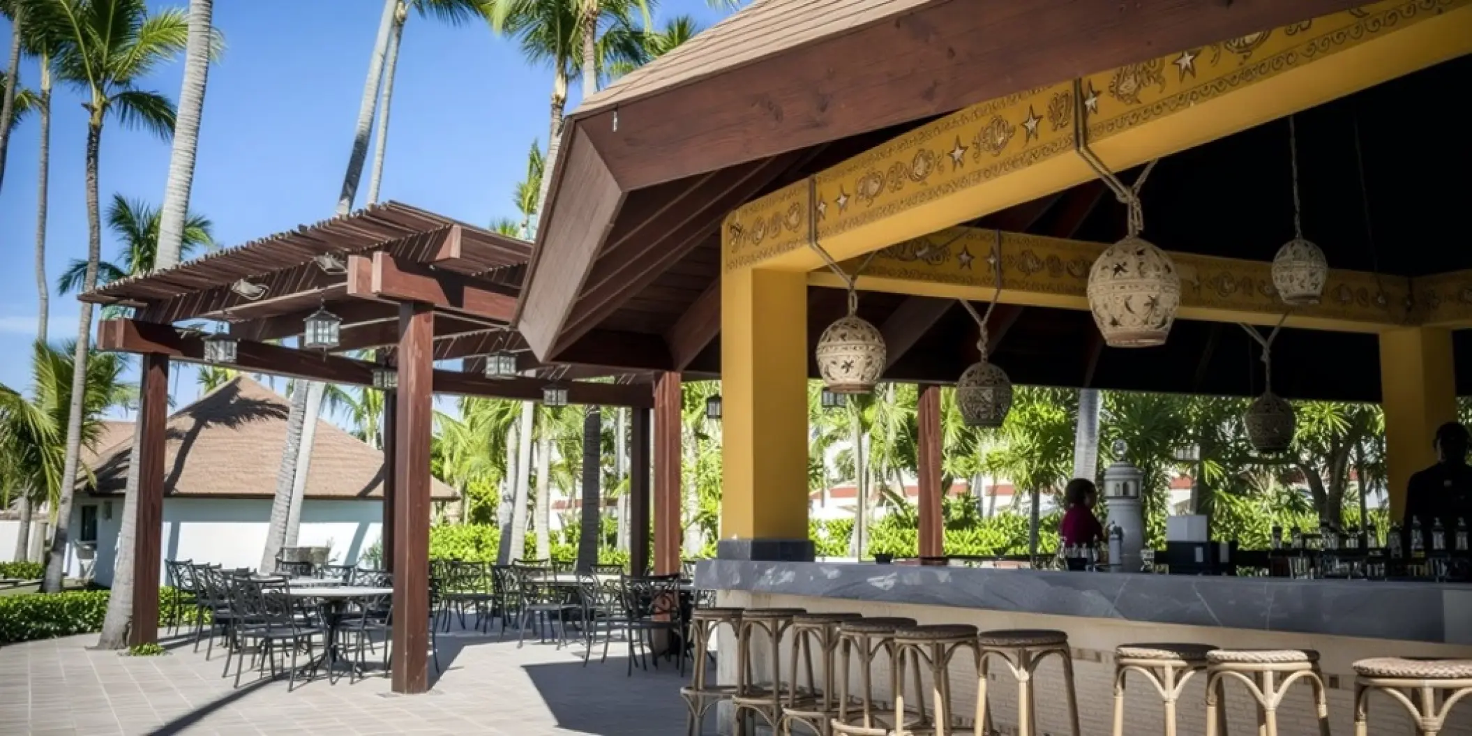 Outdoor Parrots Bar with wooden stools and terrace seating at Majestic Colonial, Punta Cana