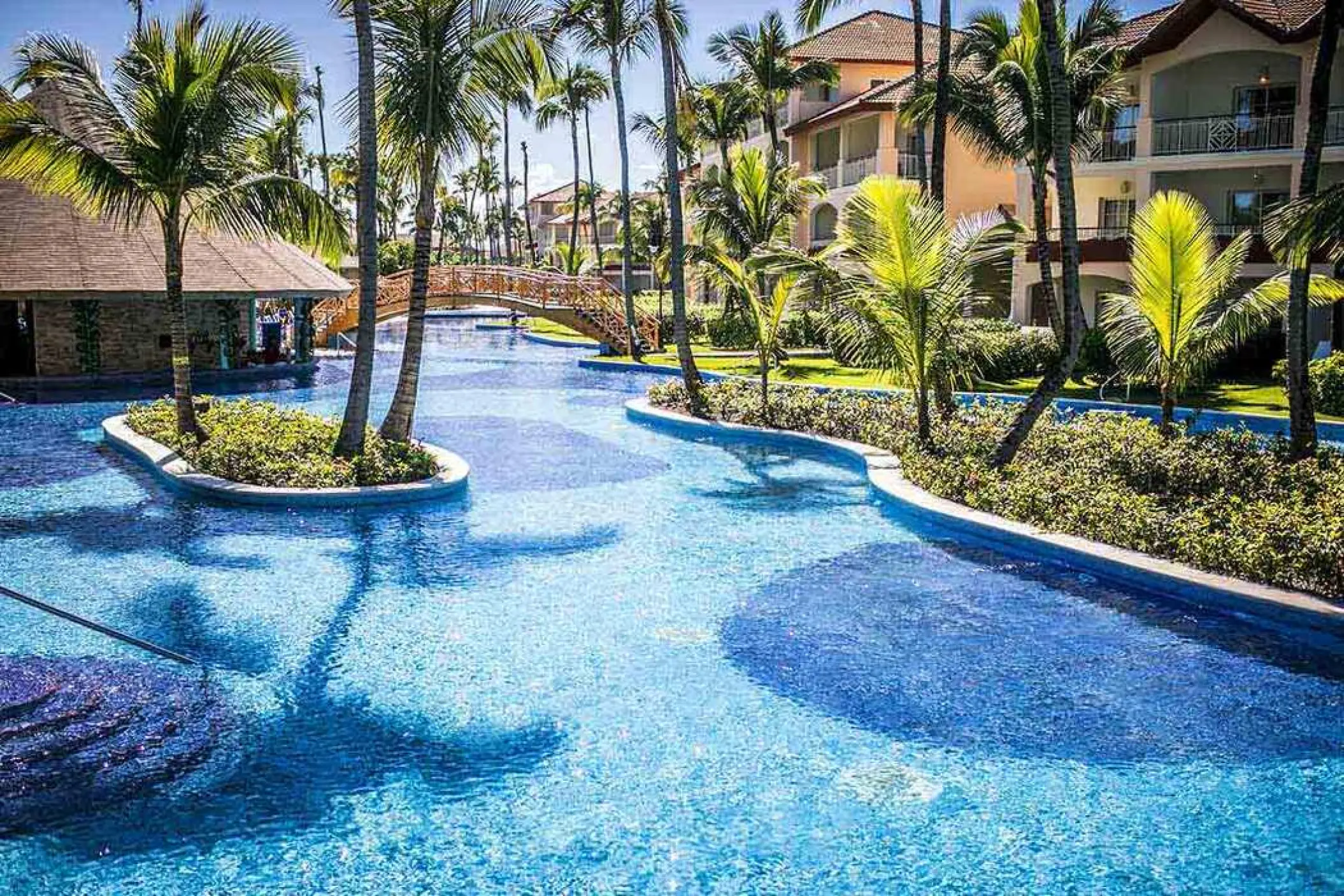 Winding lagoon pool with palm trees and a footbridge at Majestic Colonial, Punta Cana