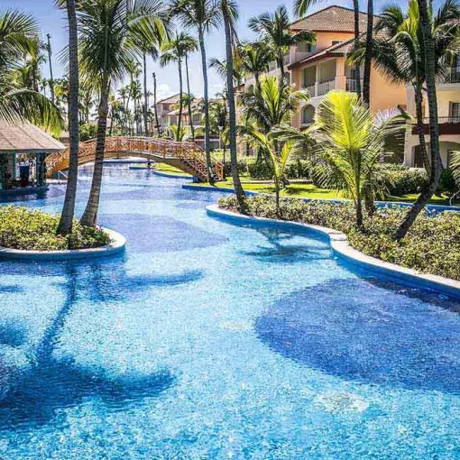 Winding lagoon pool with palm trees and a footbridge at Majestic Colonial, Punta Cana