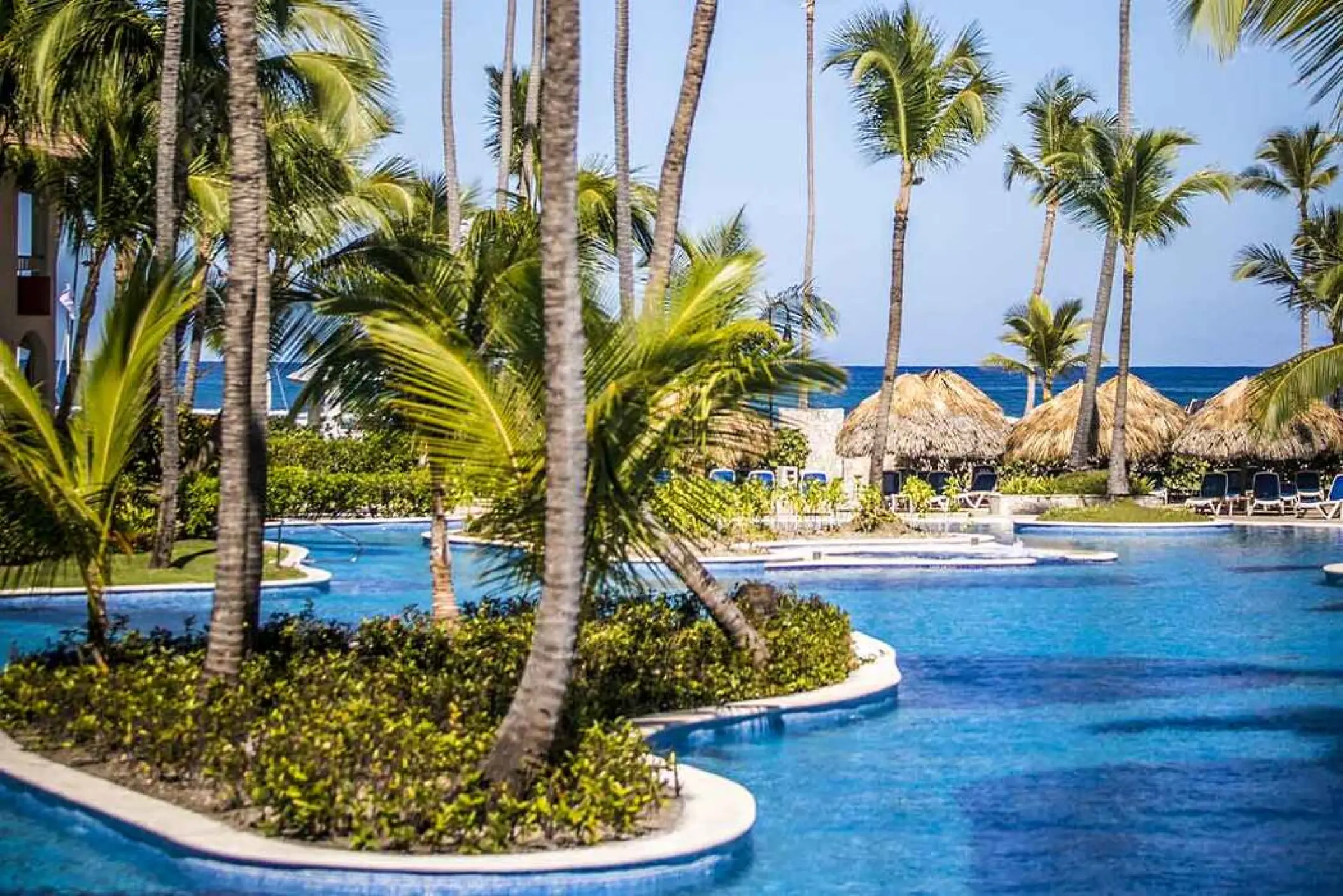 Large swimming pool surrounded by palm trees and palapas at Majestic Colonial, Punta Cana