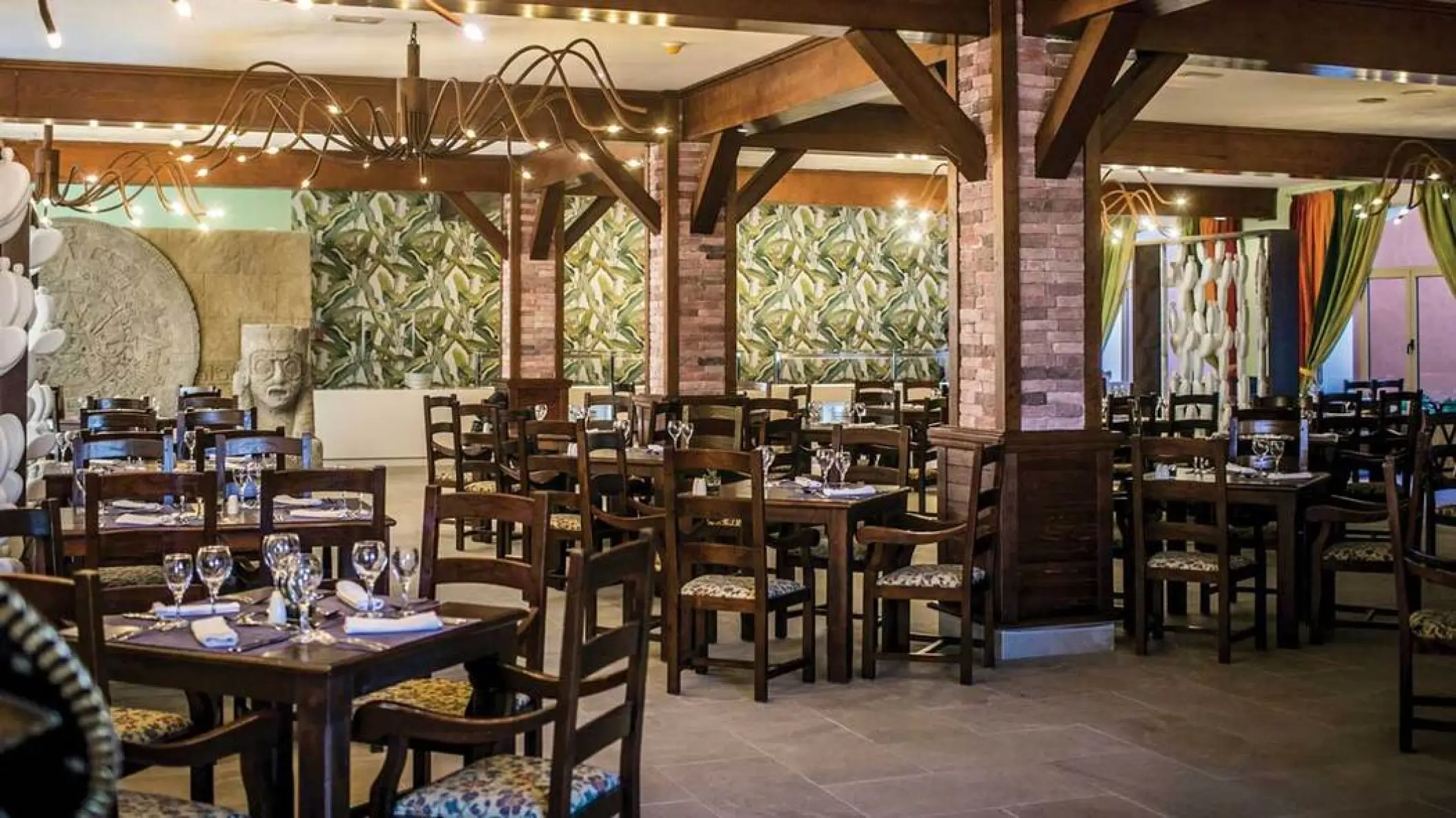 Rustic indoor restaurant with wooden tables and brick columns at Majestic Colonial, Punta Cana