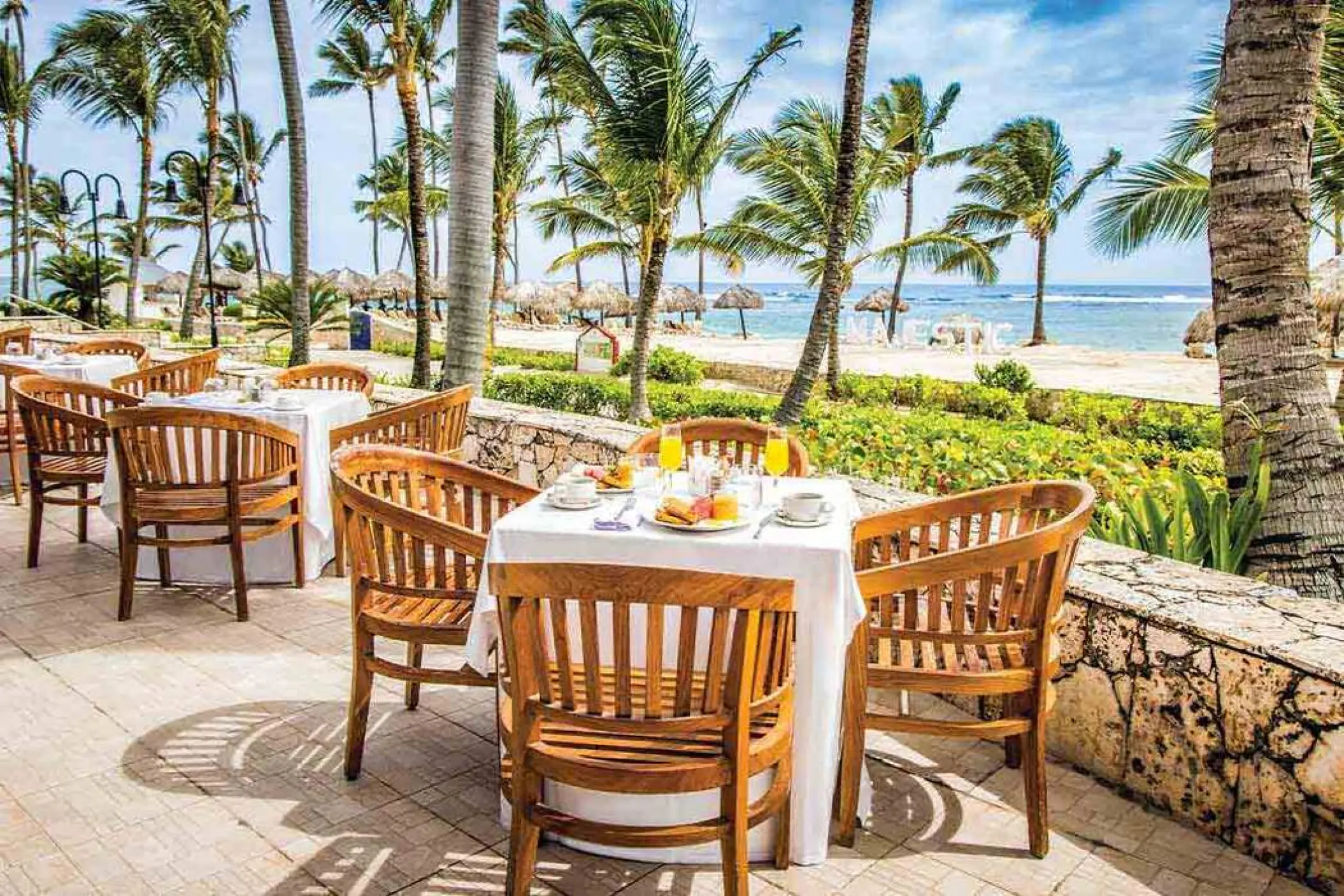 Seaside restaurant patio with wooden chairs overlooking the beach at Majestic Colonial, Punta Cana