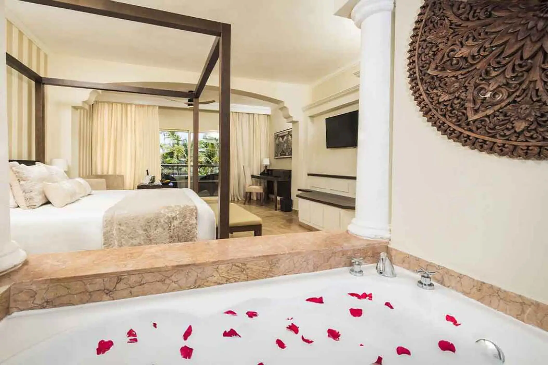 Majestic Colonial Punta Cana suite with a four-poster bed and rose petals in a hot tub, Punta Cana