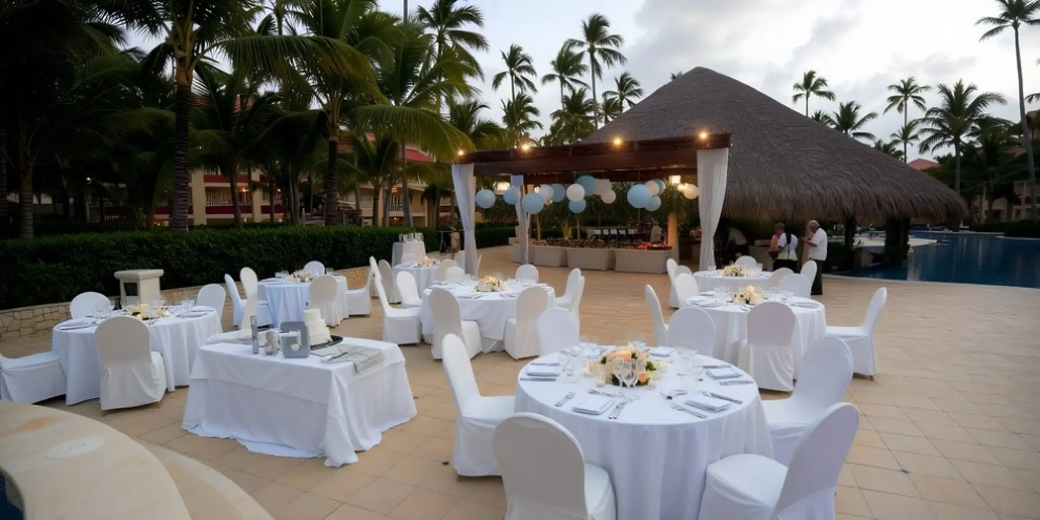 Poolside wedding reception at Majestic Colonial, Punta Cana with white tables and a thatched palapa bar