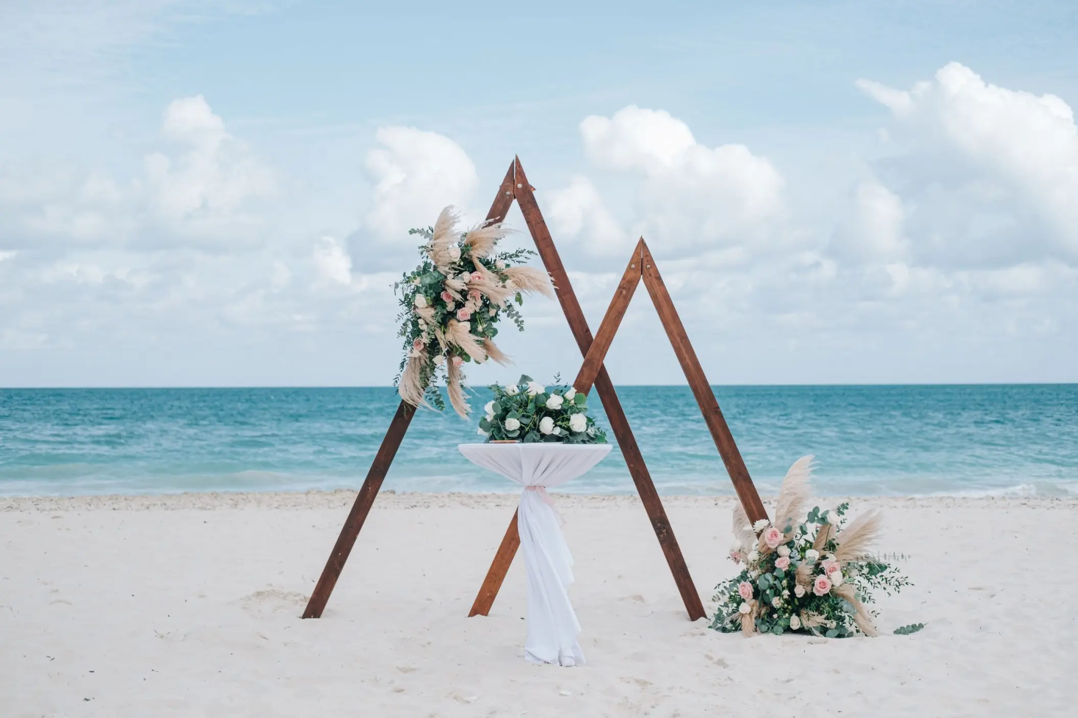 Triangular wooden wedding arch with pampas grass on the beach at Majestic Mirage Costa Mujeres, Cancun