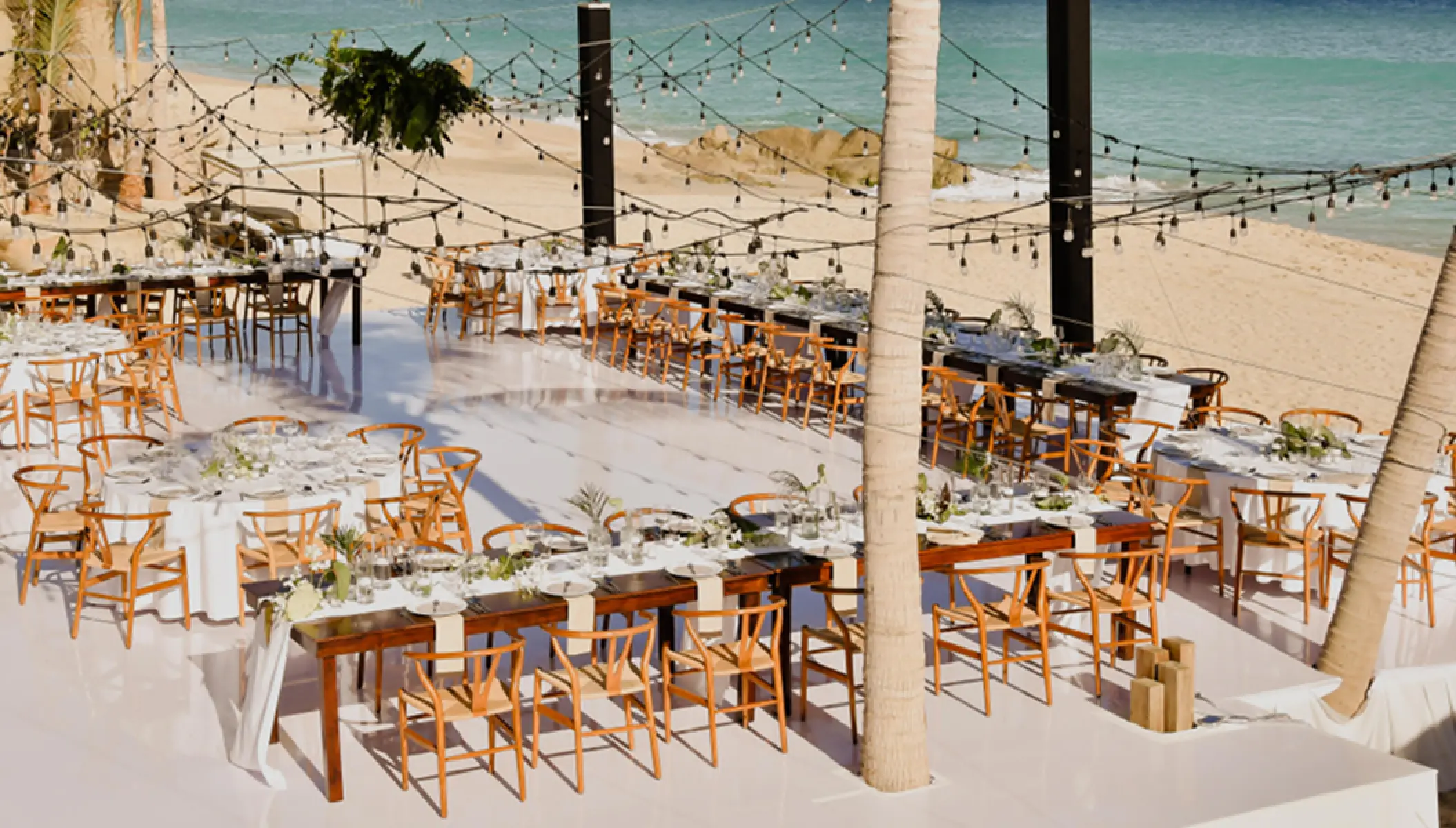Beachfront wedding reception setup with string lights and wooden chairs at Mar Del Cabo, Cabo San Lucas