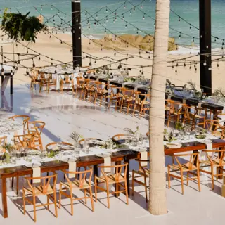 Beachfront wedding reception setup with string lights and wooden chairs at Mar Del Cabo, Cabo San Lucas