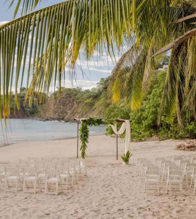 Beachfront wedding ceremony setup with white chairs and floral arch at Margaritaville Playa Flamingo, Liberia