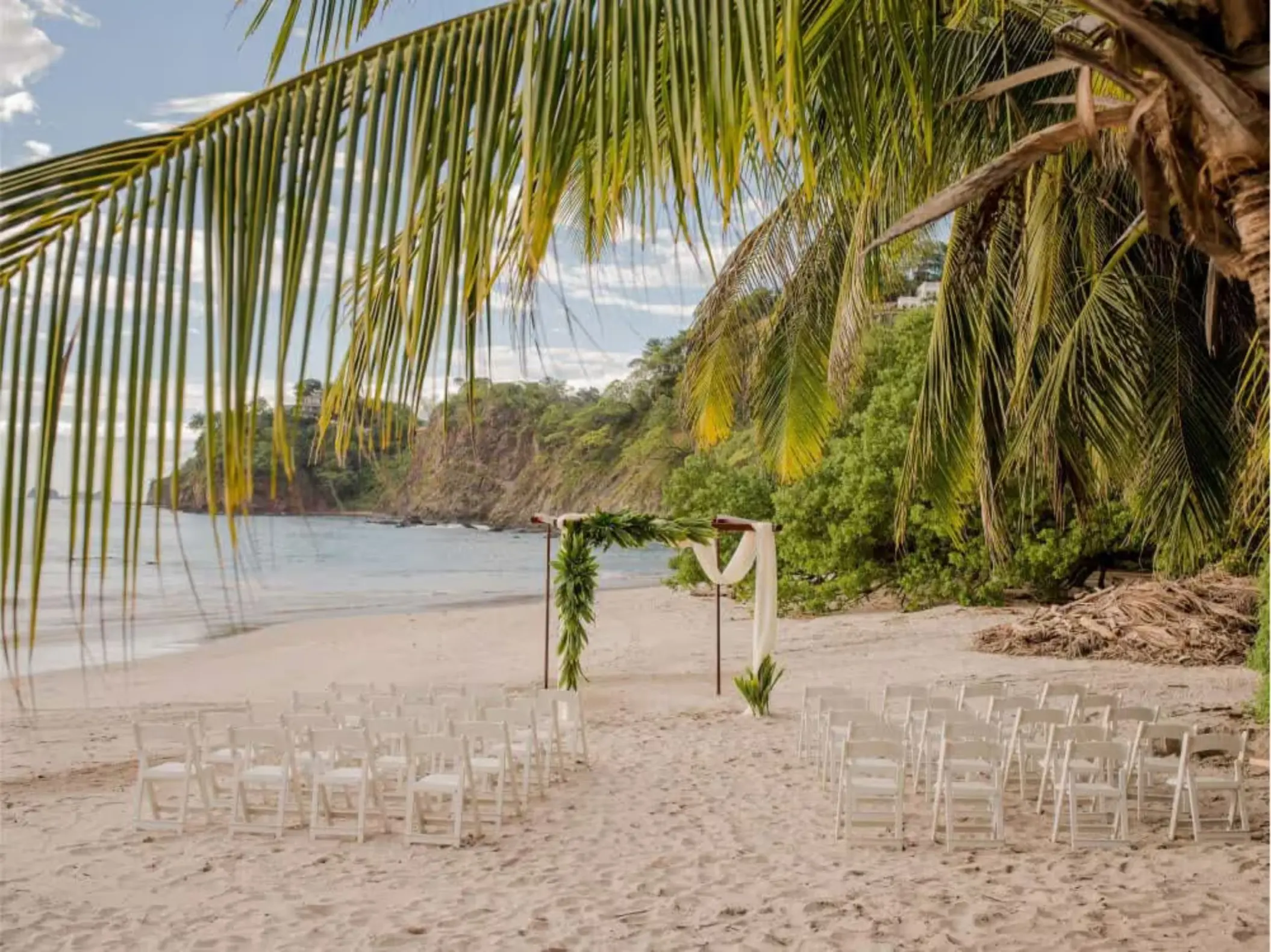 Beachfront wedding ceremony setup with white chairs and floral arch at Margaritaville Playa Flamingo, Liberia