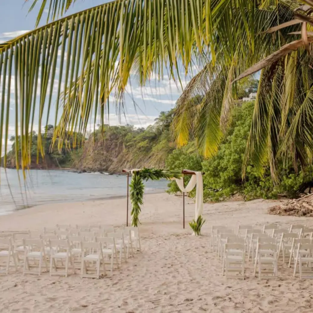 Beachfront wedding ceremony setup with white chairs and floral arch at Margaritaville Playa Flamingo, Liberia