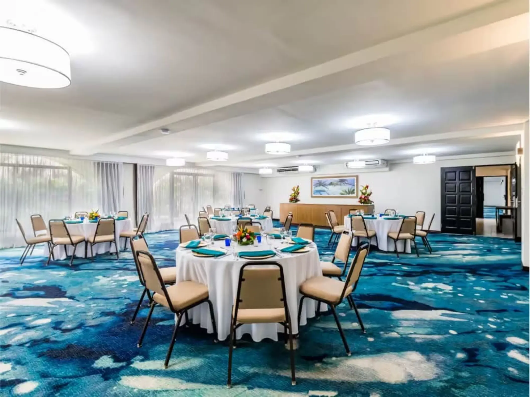 Indoor reception setup with round tables and patterned blue carpet at Margaritaville Beach Resort Playa Flamingo