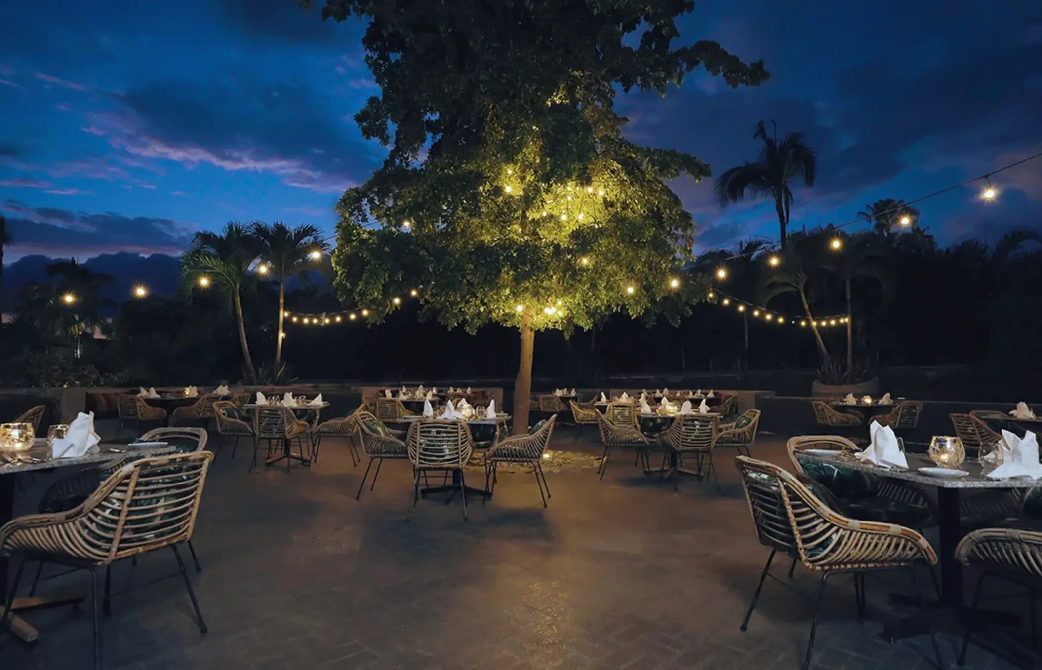 Outdoor restaurant terrace at night with string lights and woven chairs at Armony Marival, Puerto Vallarta