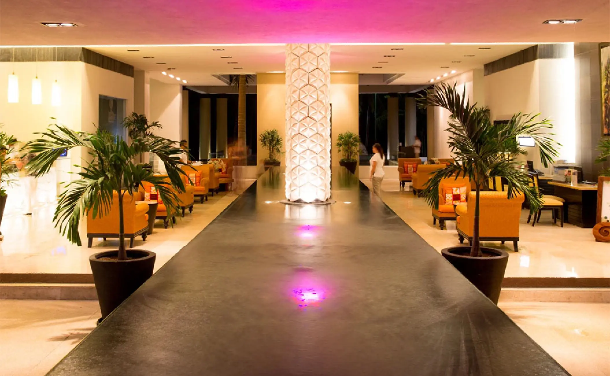 Modern open-air lobby with orange armchairs and a lit decorative pillar at Marival Distinct, Puerto Vallarta