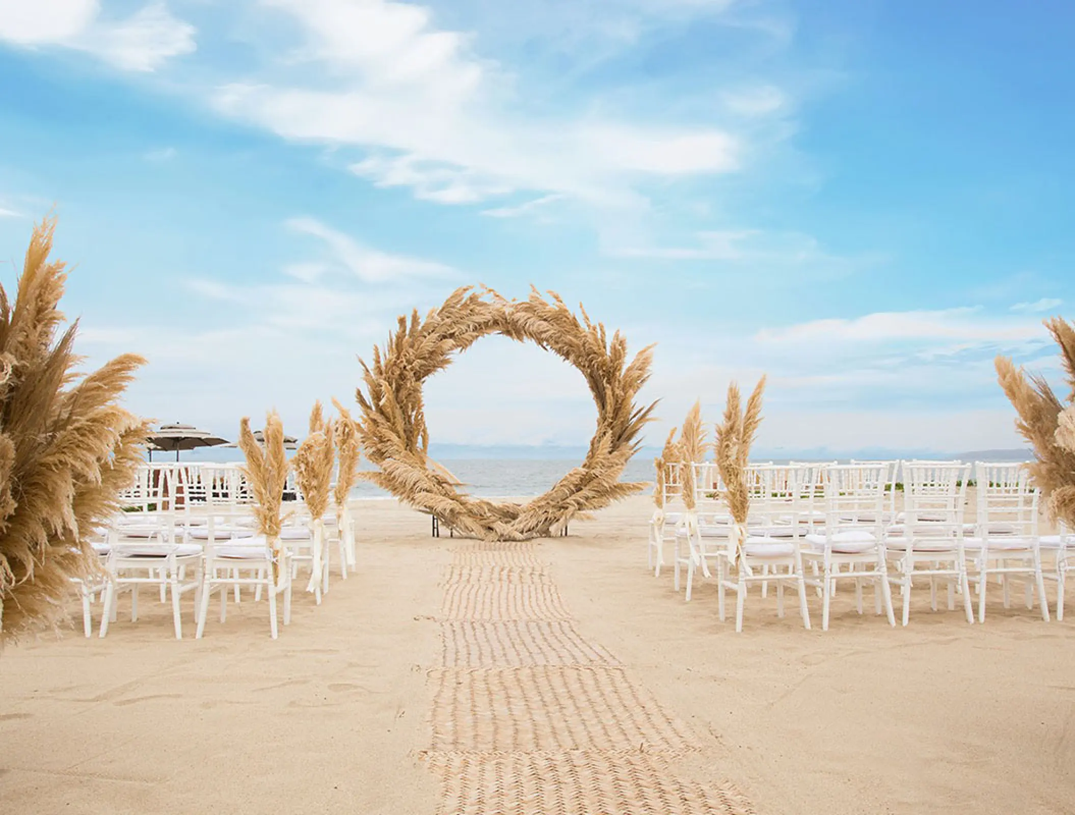 Beachfront wedding ceremony with pampas grass arch and white chairs at Marival Distinct, Puerto Vallarta