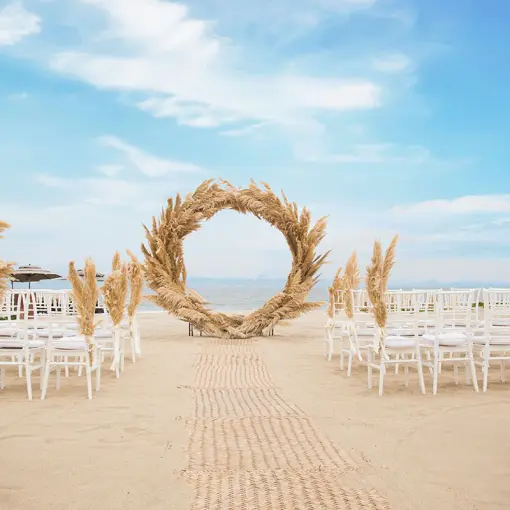 Beachfront wedding ceremony with pampas grass arch and white chairs at Marival Distinct, Puerto Vallarta