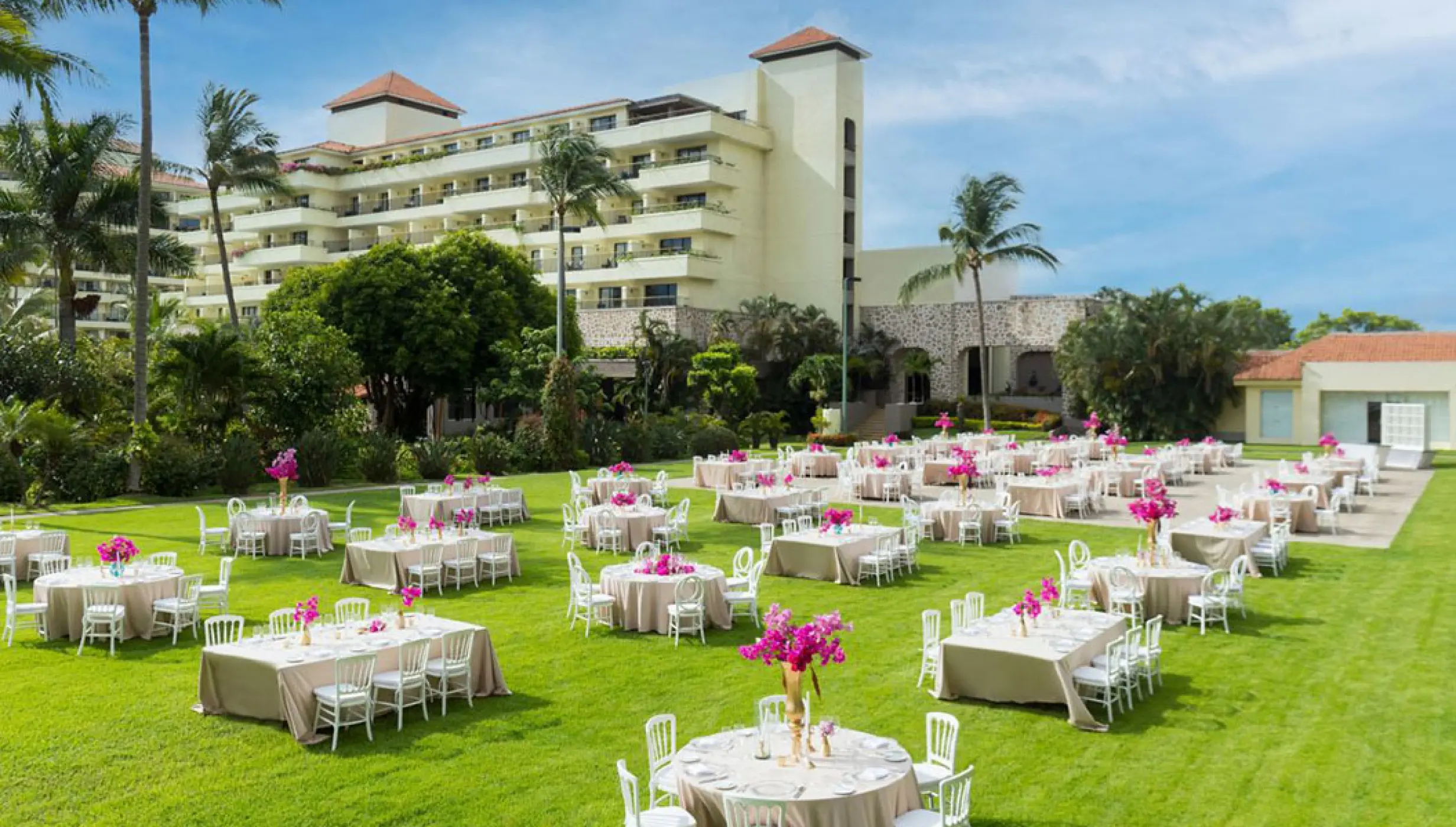 Garden wedding reception at Marriott Puerto Vallarta with round tables, pink floral centerpieces, and white chairs