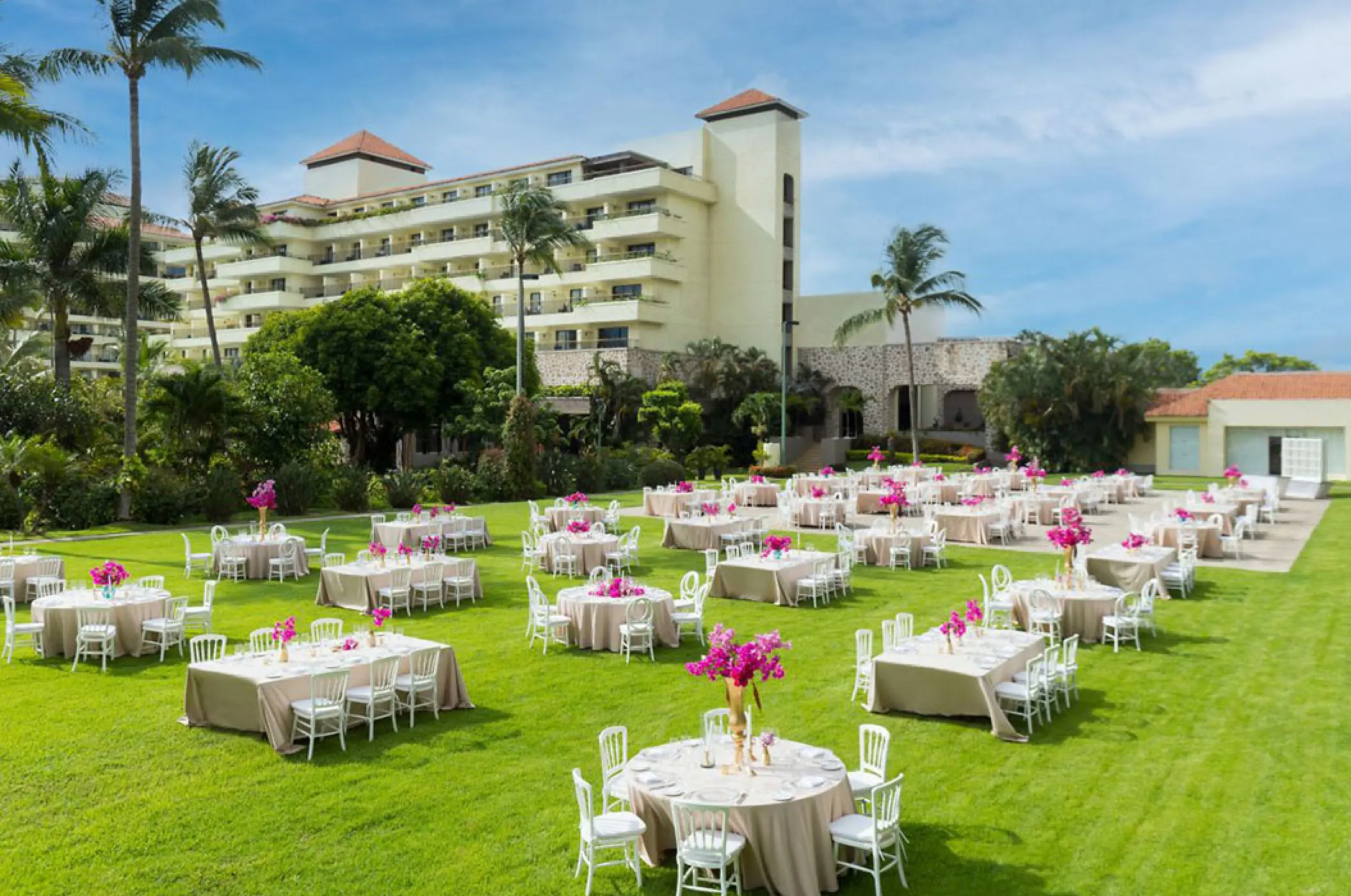 Garden wedding reception at Marriott Puerto Vallarta with round tables, pink floral centerpieces, and white chairs
