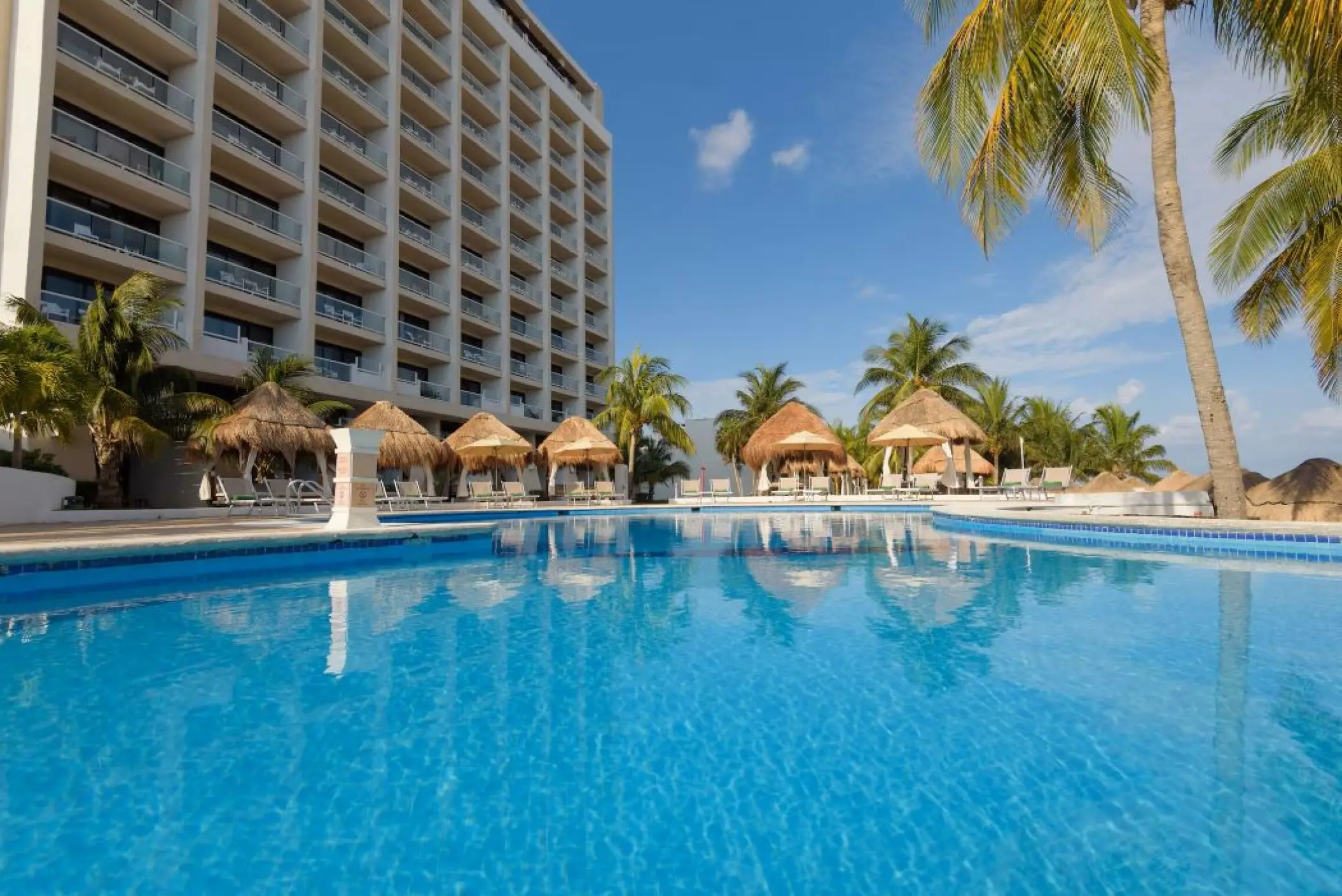 Melia Cozumel outdoor swimming pool with thatched umbrellas and resort building, Cozumel
