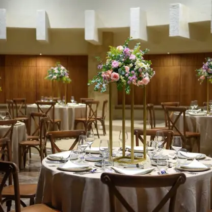 Indoor wedding reception with tall floral centerpieces and wooden cross-back chairs at Melia Cozumel